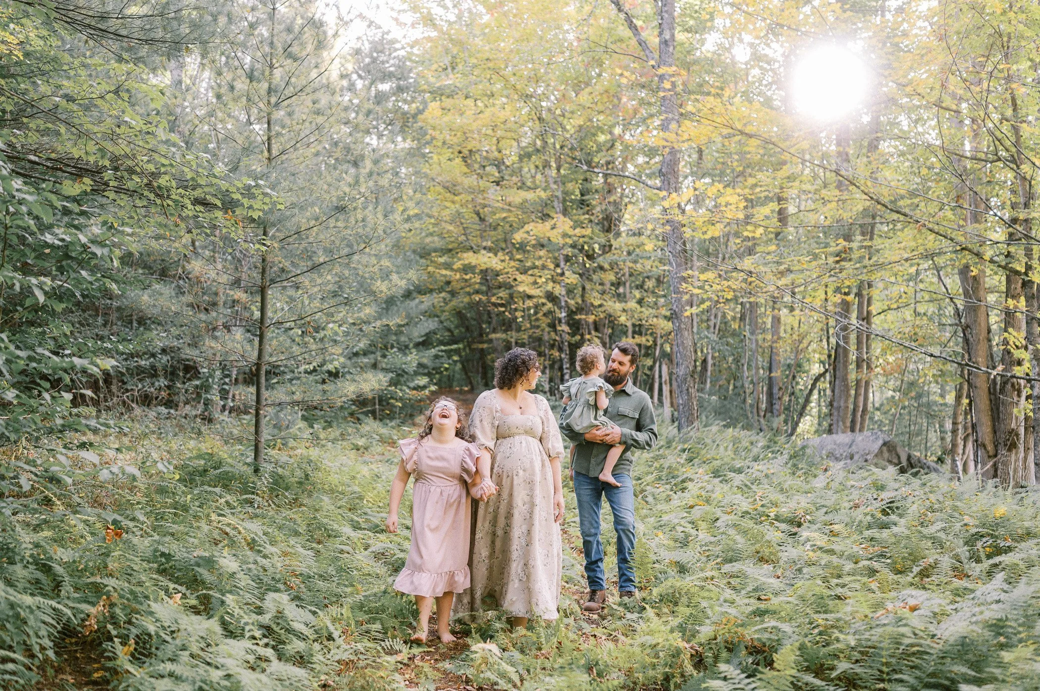 A family of four walking and enjoying nature in a forest, with sunlight filtering through trees.