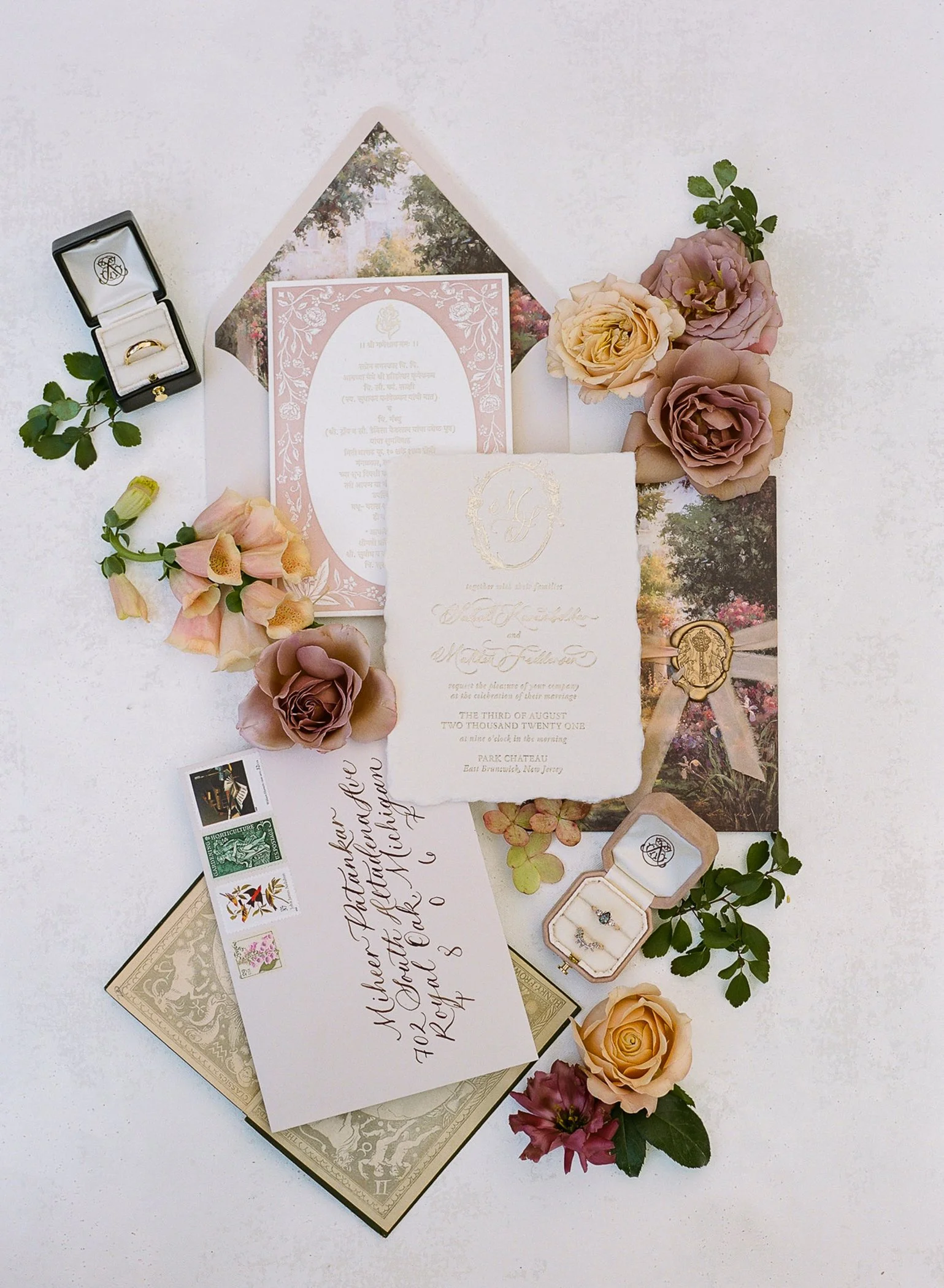 Wedding invitation, ring box with engagement ring, vintage postcards, floral arrangements, and handwritten envelope on a white surface.