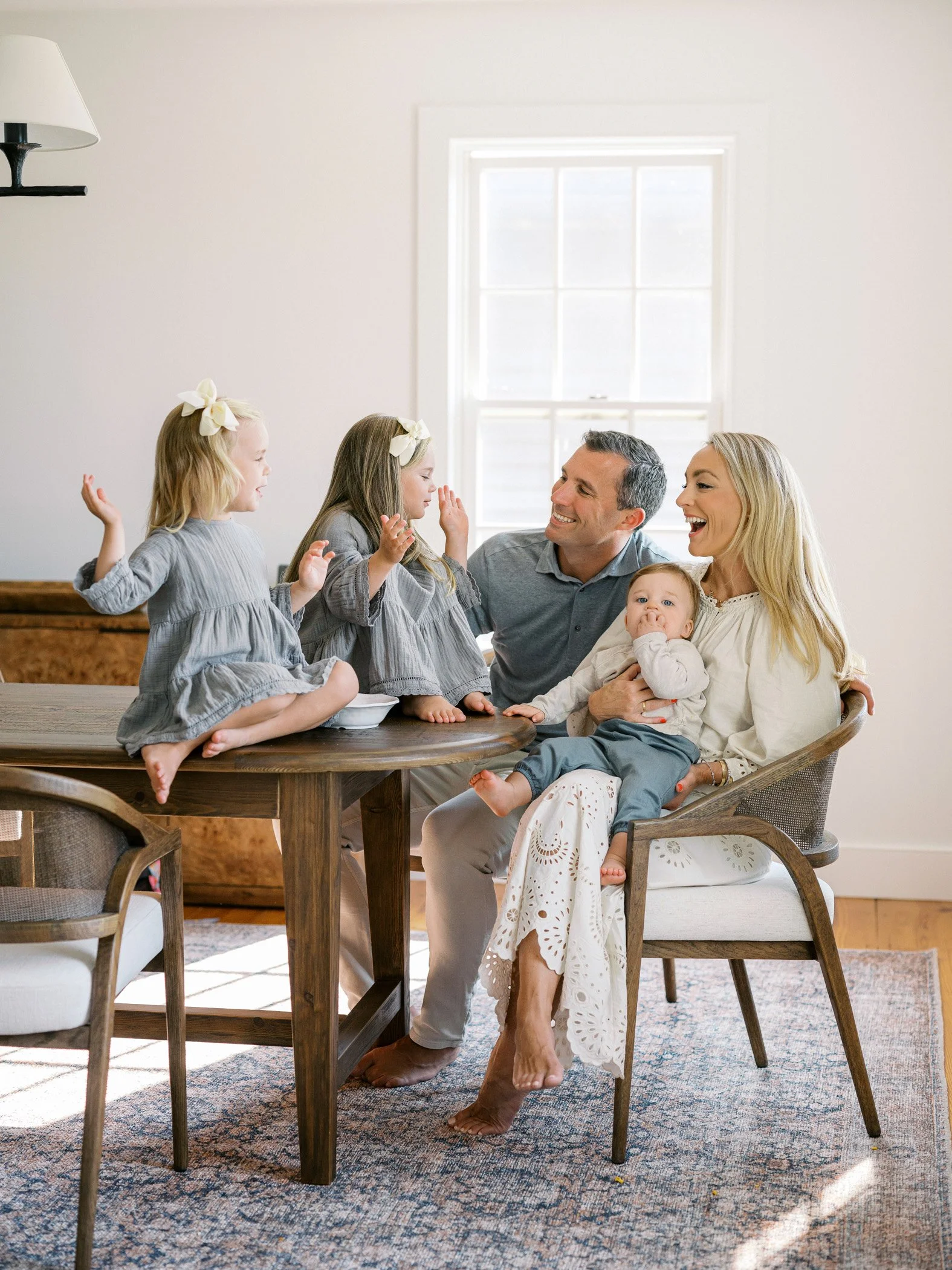 Family of six, including two adults and four children, gathered around a table in a bright room, smiling and playing.