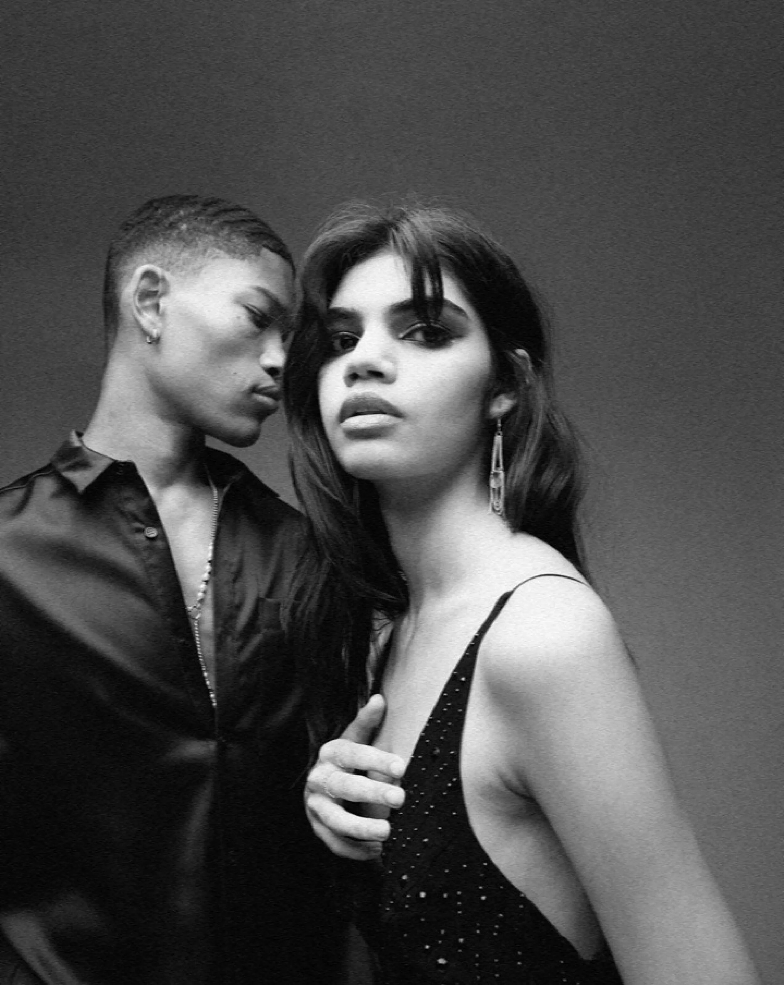 Black and white photo of two women, one with short hair and earrings, and the other with long hair and carrying a purse, posing close together.