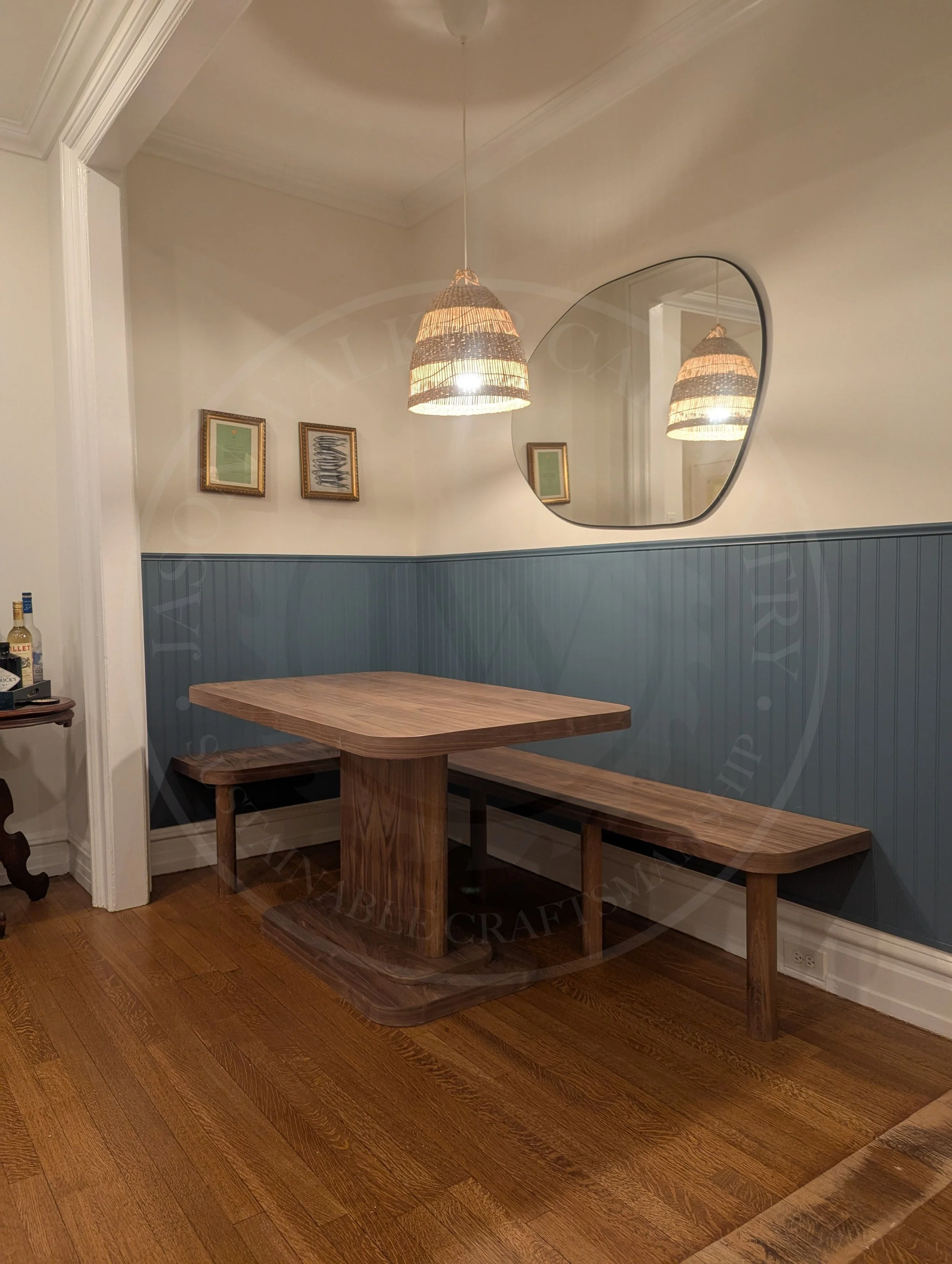 Custom walnut dining banquette with a matching pedestal table and bench seating, set against blue bead board wainscoting and cream walls