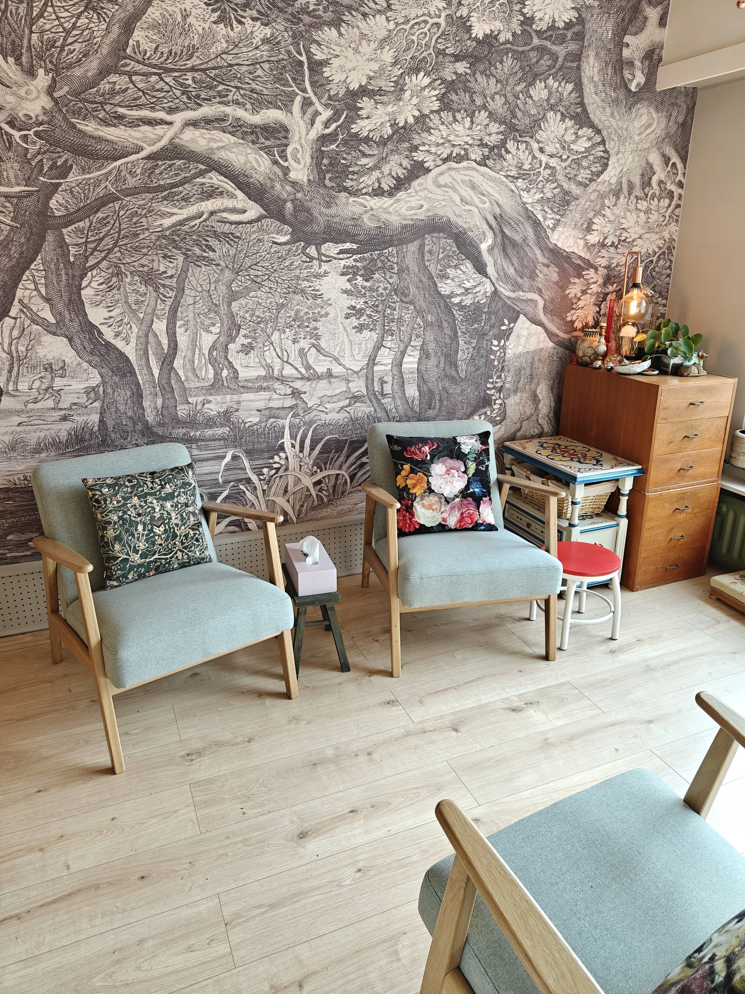 Een gezellige zithoek met twee armstoelen met lichtgroene bekleding en houten armleuningen, versierd met bloemrijke kussens.