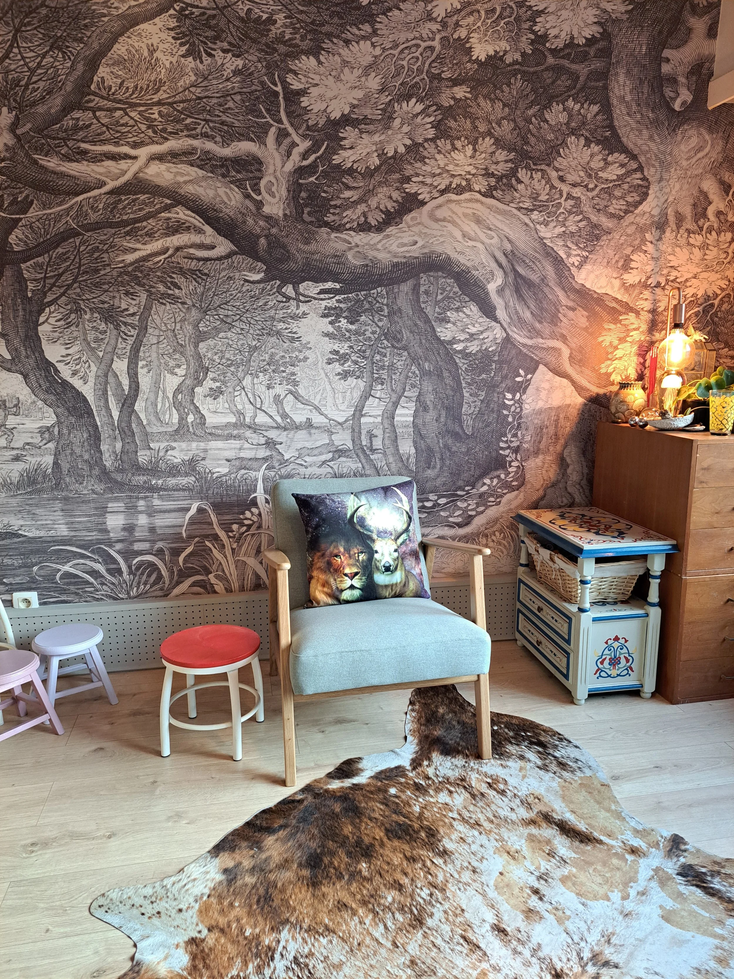 Een praktijkruimte met een grote poster van een boslandschap, een fauteuil naast een klein wit tafeltje met blauwe details en een dierenhuid op de vloer.