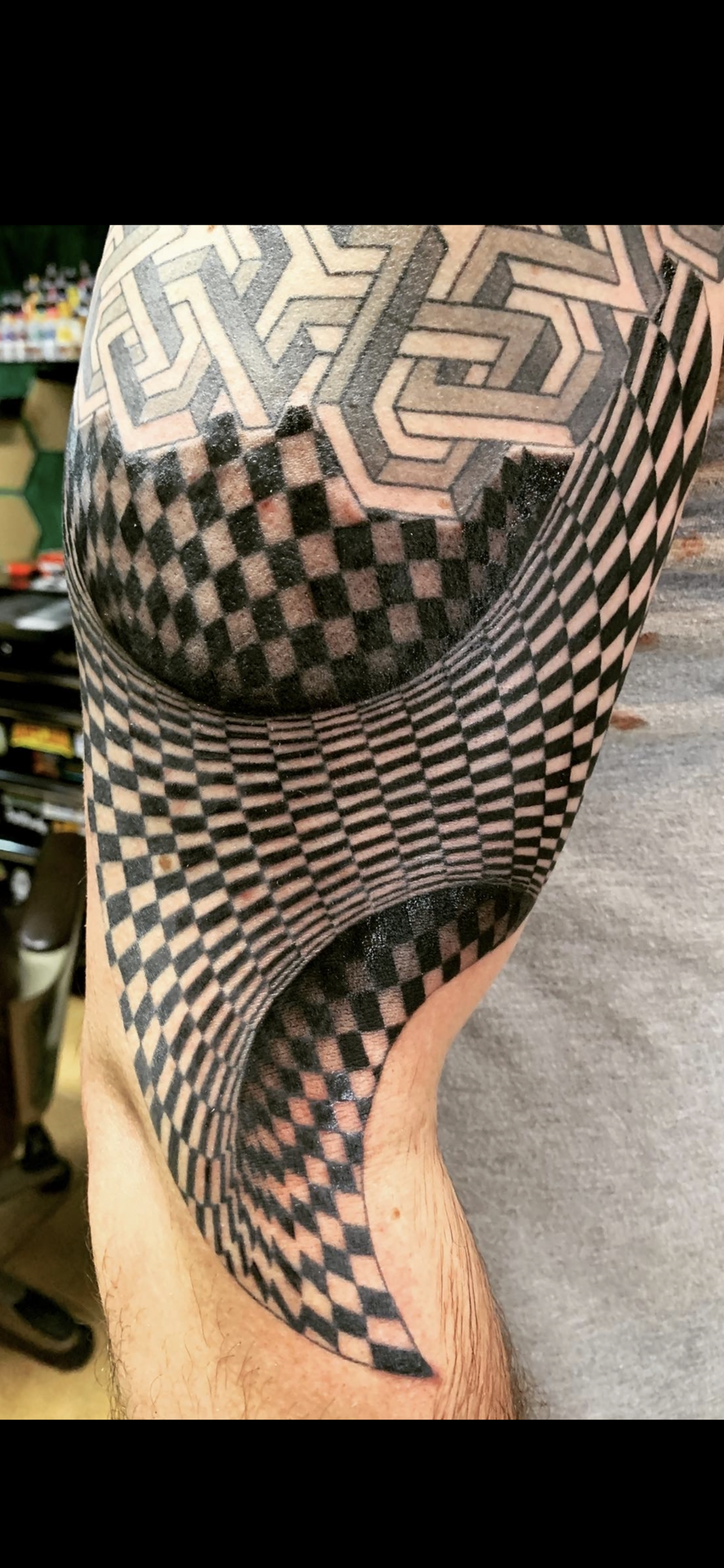 Close-up of a person's arm with a large geometric tattoo pattern featuring 3D optical illusions using black and gray ink.