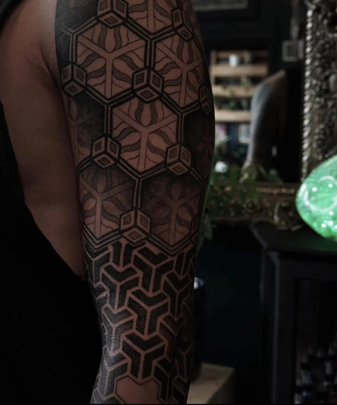 Close-up of a person's tattooed upper arm and shoulder with complex geometric black ink patterns covering the skin.