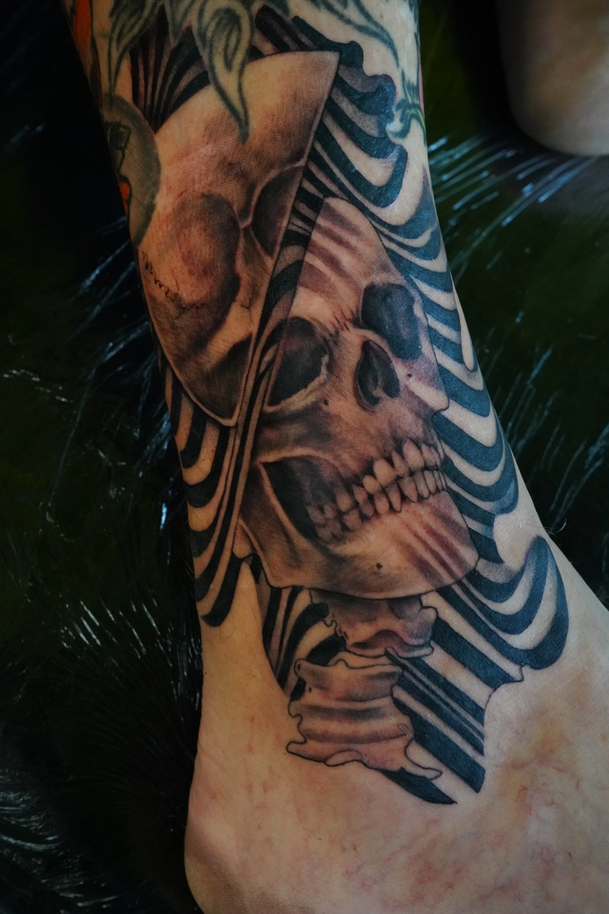 Tattoo of a human skull on a person's arm, surrounded by black and white striped patterns.