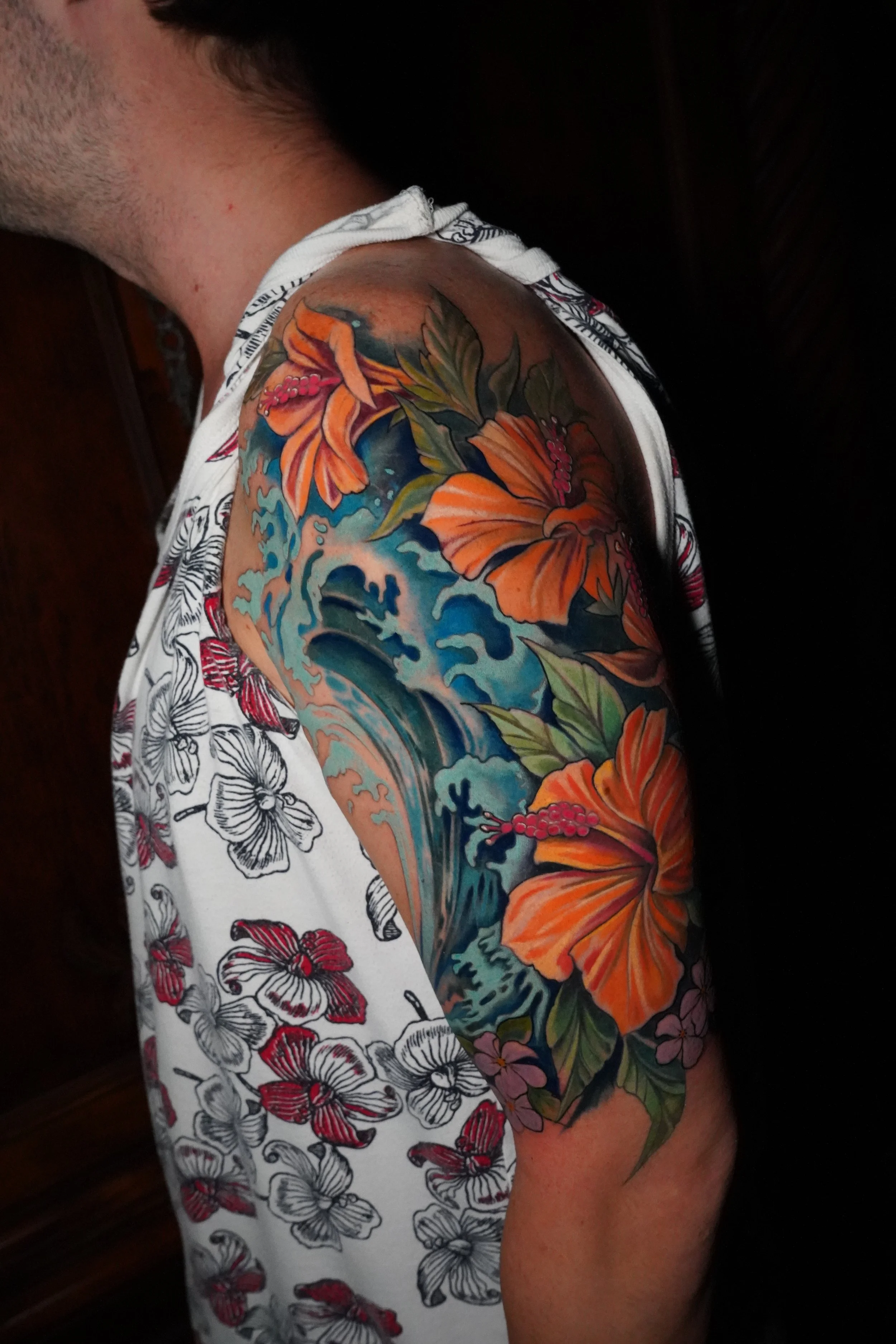 Colored tattoo of a wave and orange hibiscus flowers on a person's upper arm.