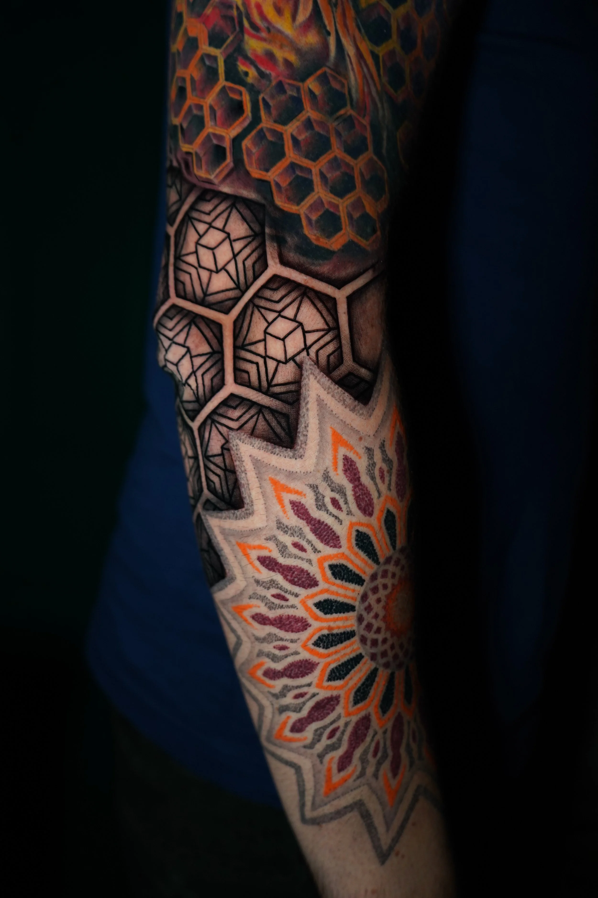 Close-up of a person's arm with colorful geometric tattoos, including hexagon and star patterns.