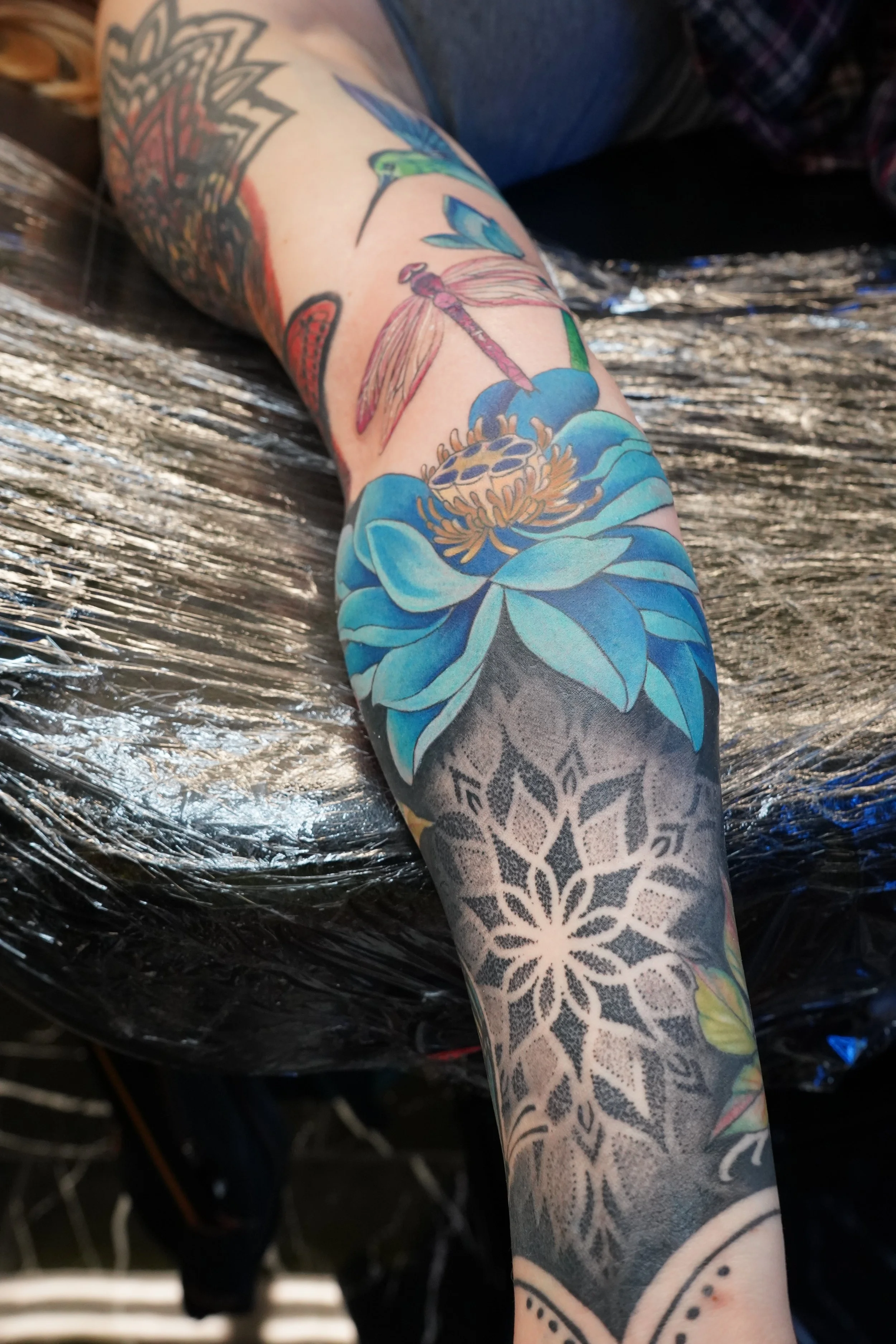 Colorful tattoo sleeve featuring a blue flower, a pink dragonfly, and a black and grey geometric pattern.