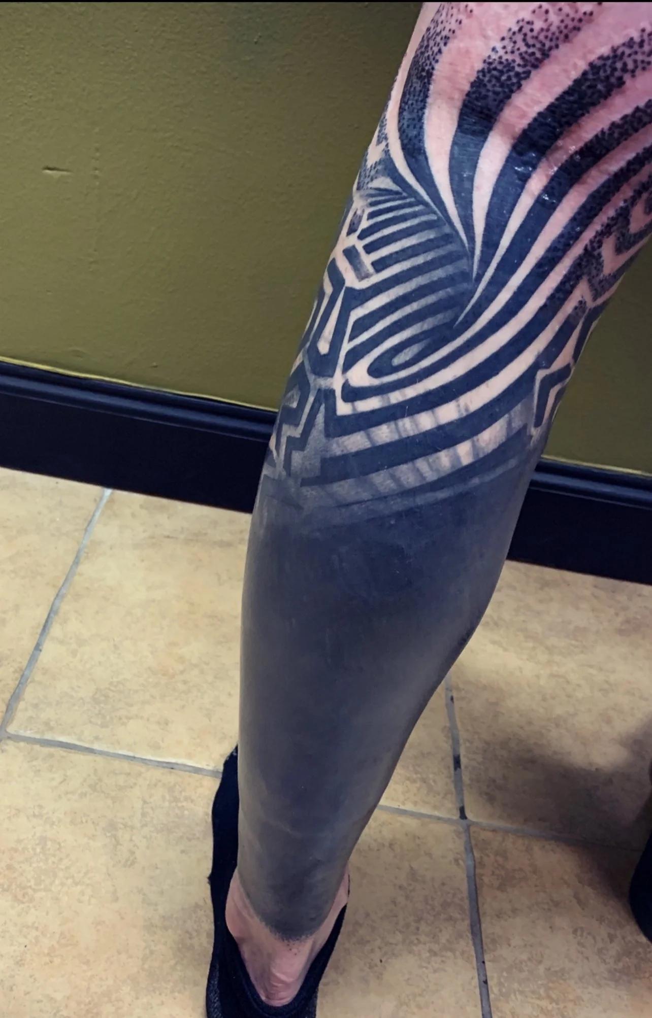 Close-up of a person's leg with a large tattoo sleeve, featuring geometric and abstract patterns in black ink.