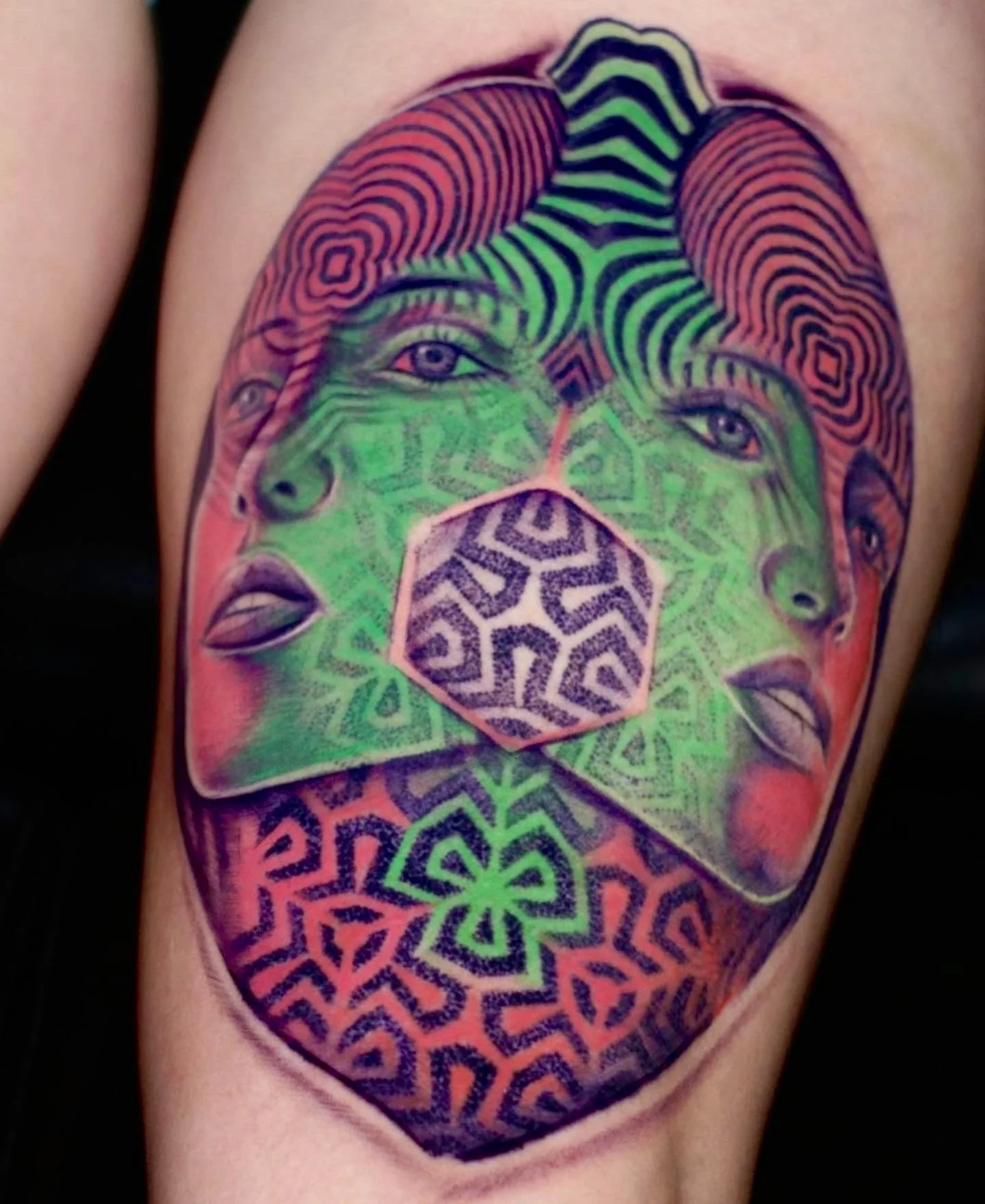 Colorful tattoo of a surreal face with multiple eyes, lips, and abstract patterns, including a central geometric shape.