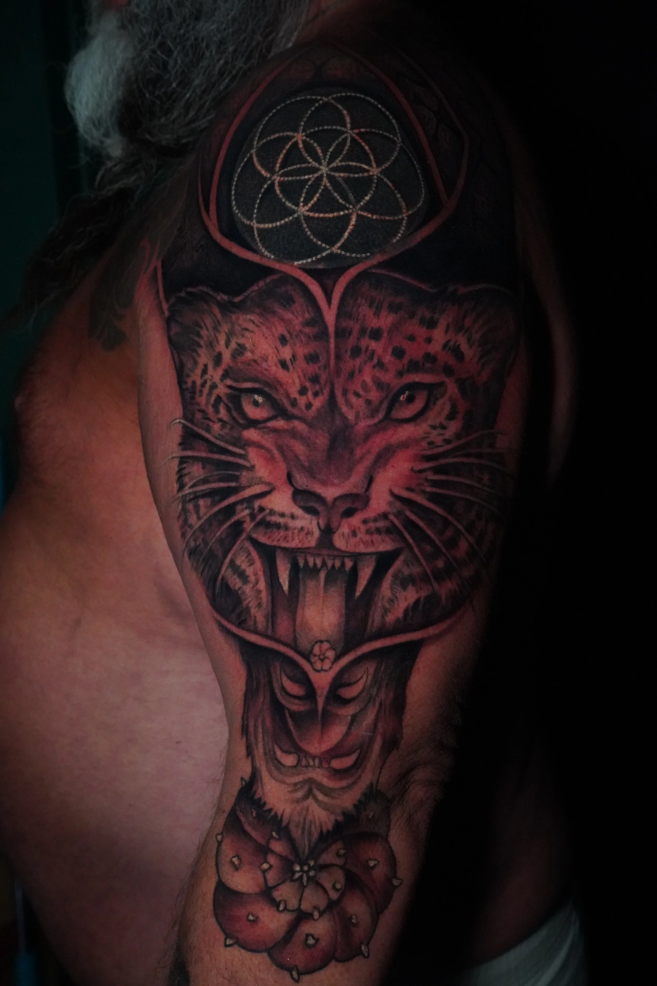 Tattoo of a snarling big cat, possibly a jaguar or leopard, with sharp teeth and piercing eyes, surrounded by floral and geometric designs.