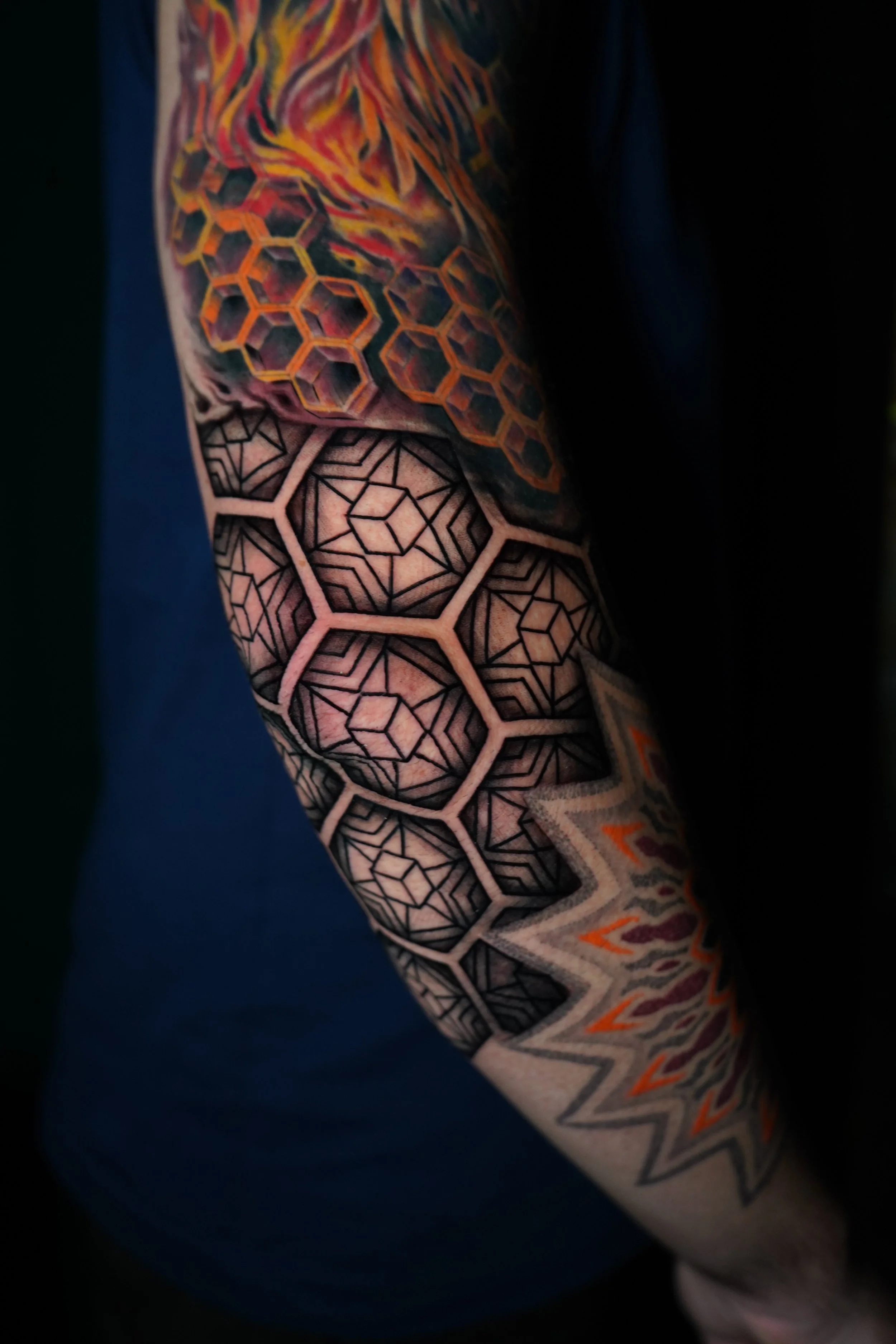 Tattoo on person's arm featuring black and gray geometric patterns and colored designs with hexagonal and star shapes.