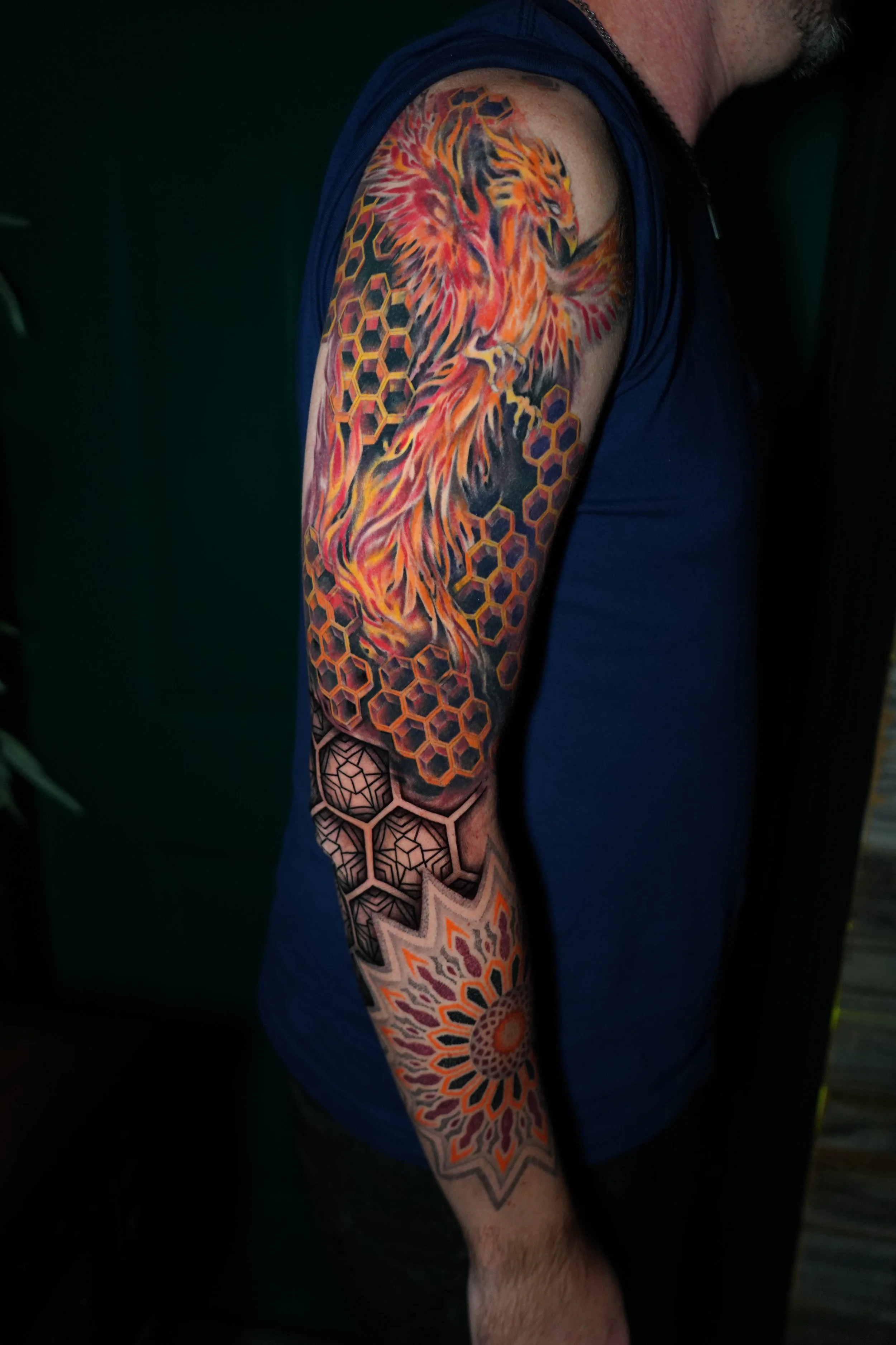 A person's arm with a colorful tattoo of a lion surrounded by geometric patterns and honeycomb designs.