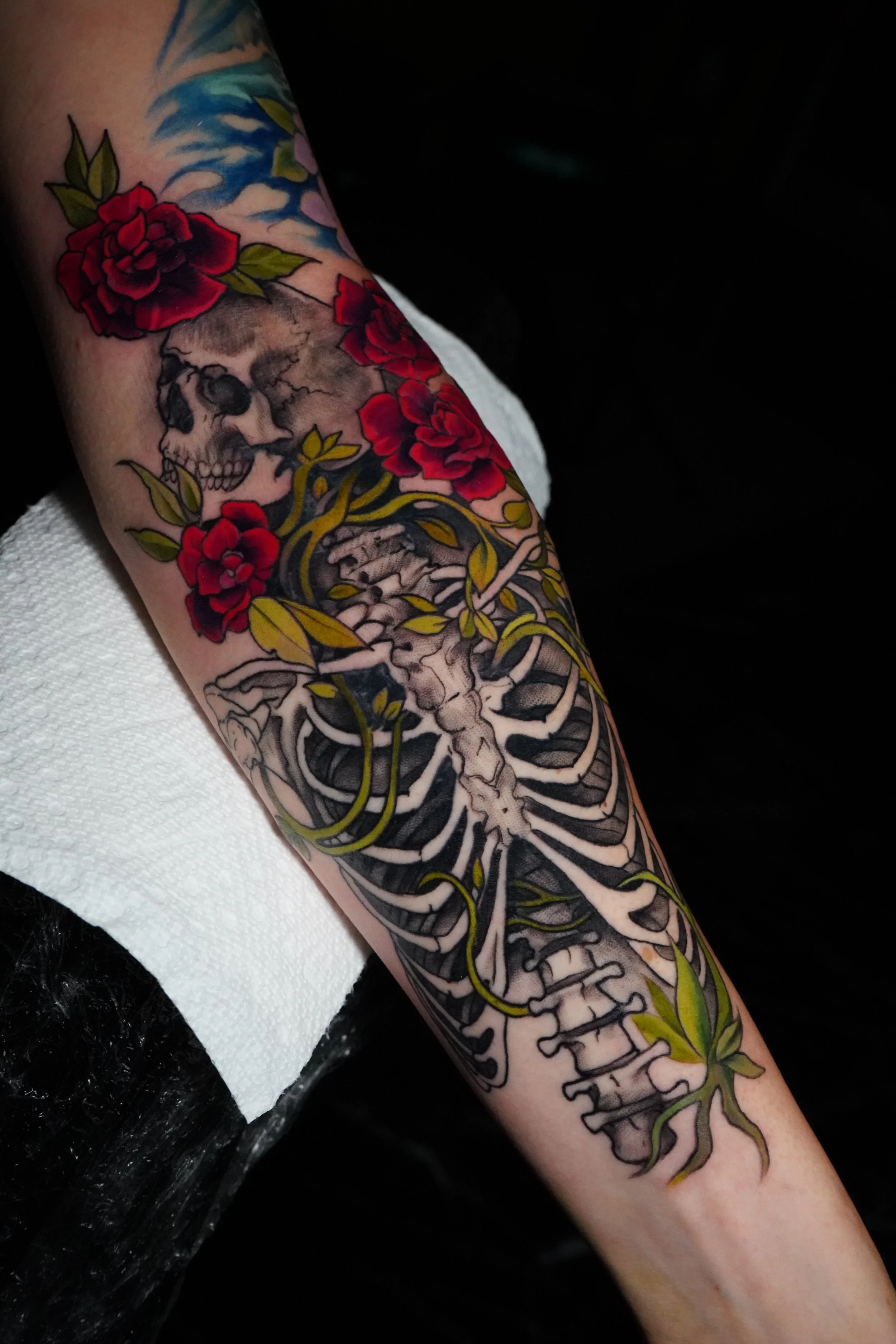 Colorful tattoo of a skull, a skeleton, and vibrant red roses on a person's arm.