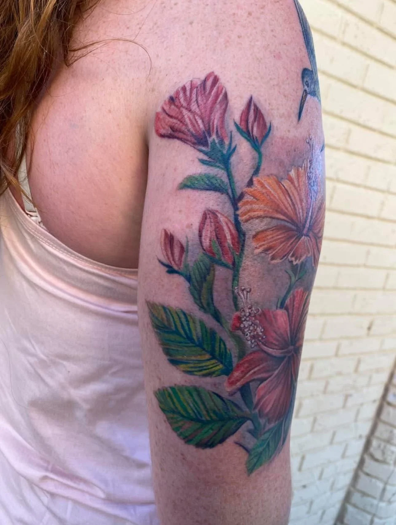 Colorful tattoo of a hibiscus flower and leaves on a person's upper arm.