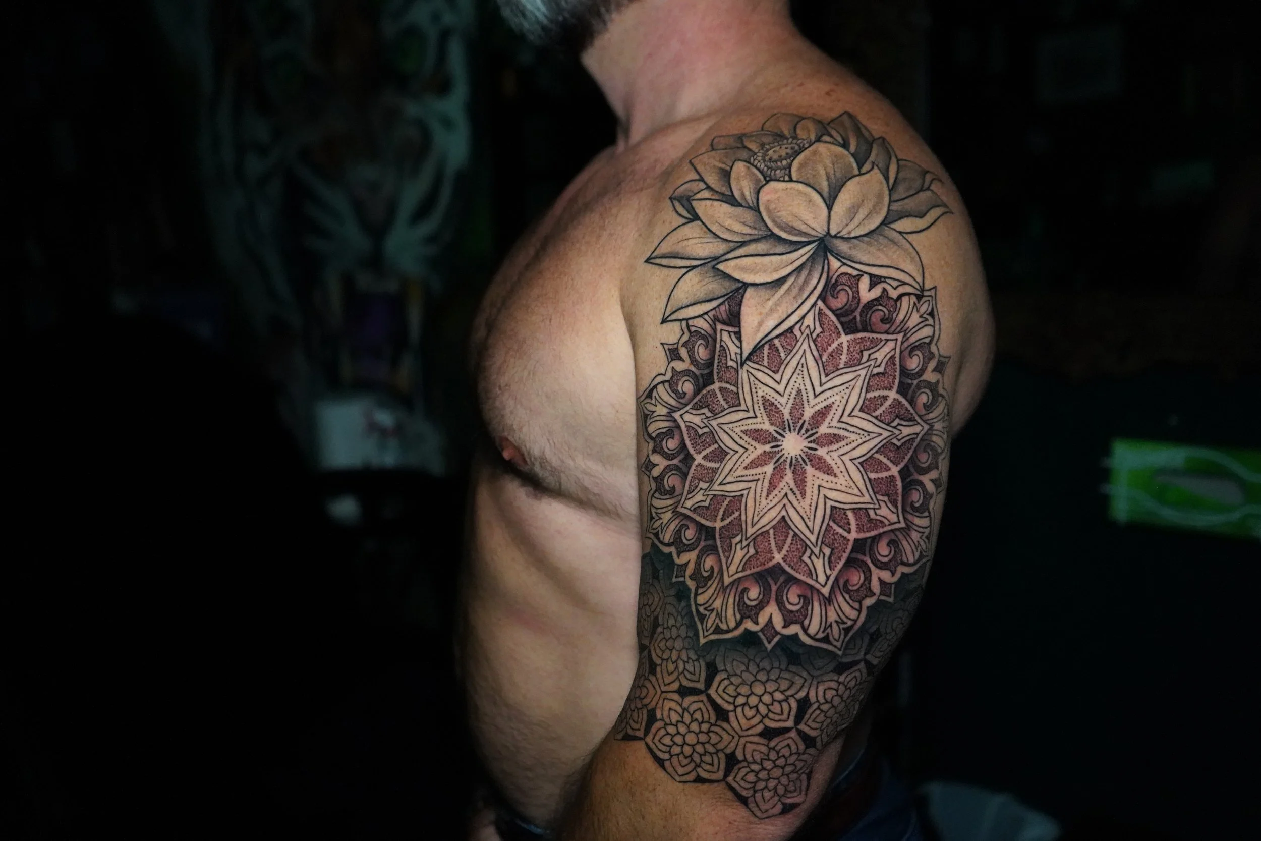 Tattoo of a large flower and geometric patterns on a man's upper arm and shoulder
