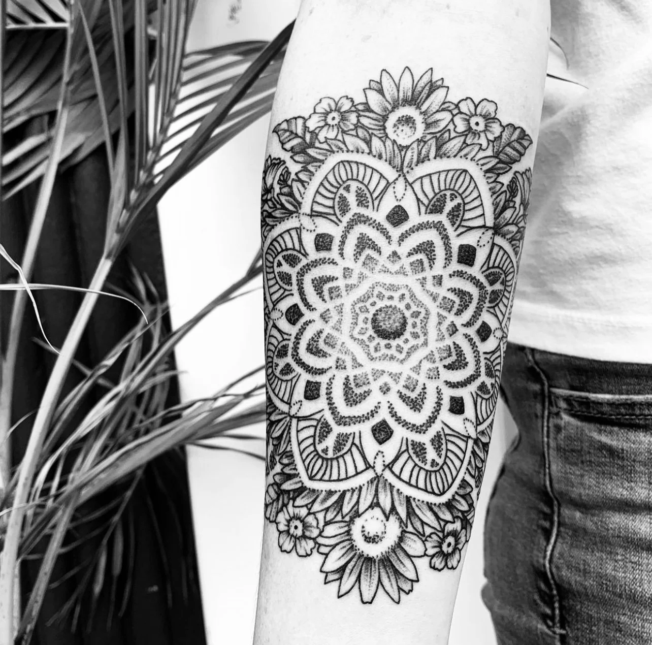 Black and white tattoo featuring a mandala with floral patterns on a person's forearm.