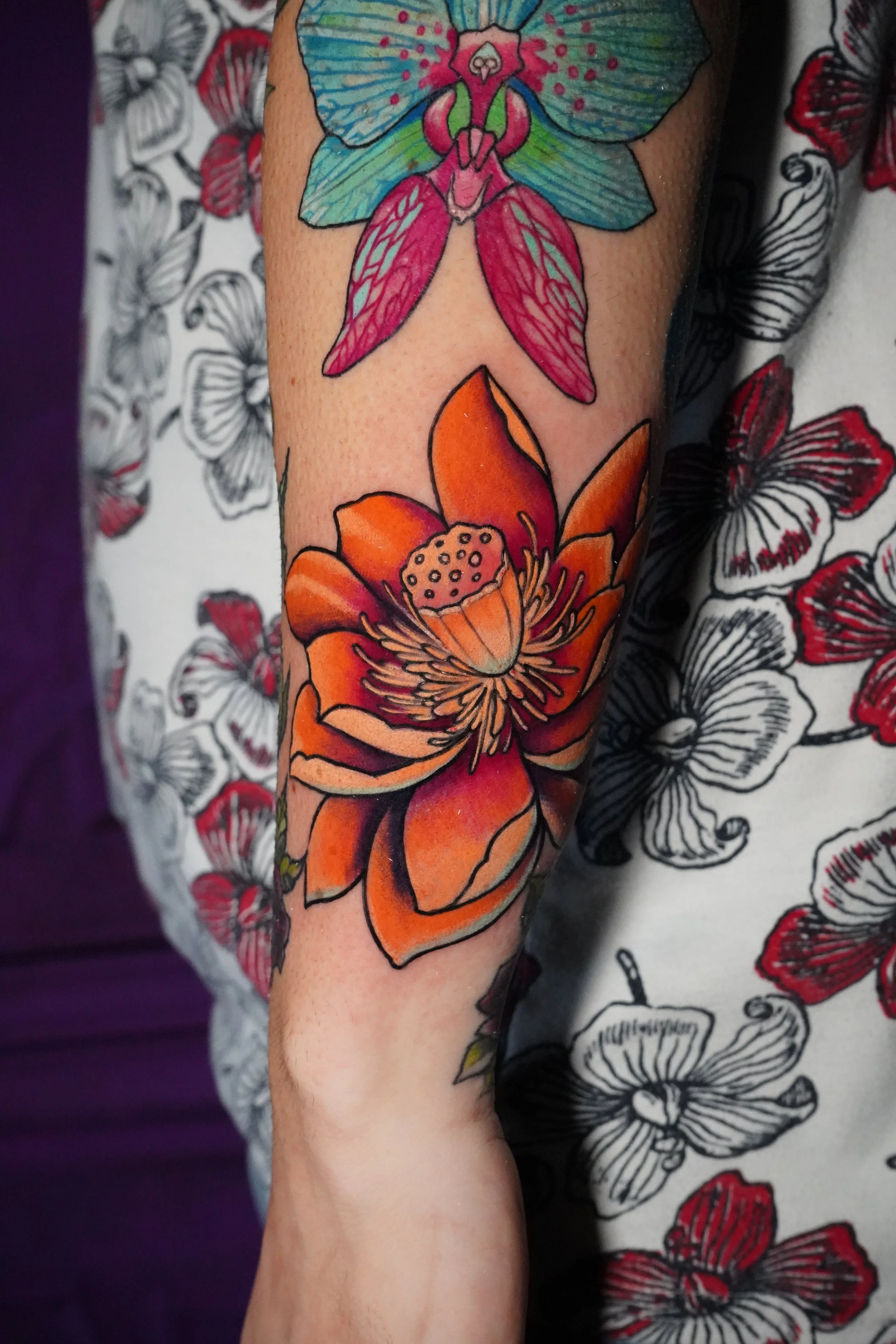 A colorful tattoo of a butterfly and a large orange flower on a person's arm, with a background of black and red butterfly patterns on a white shirt.