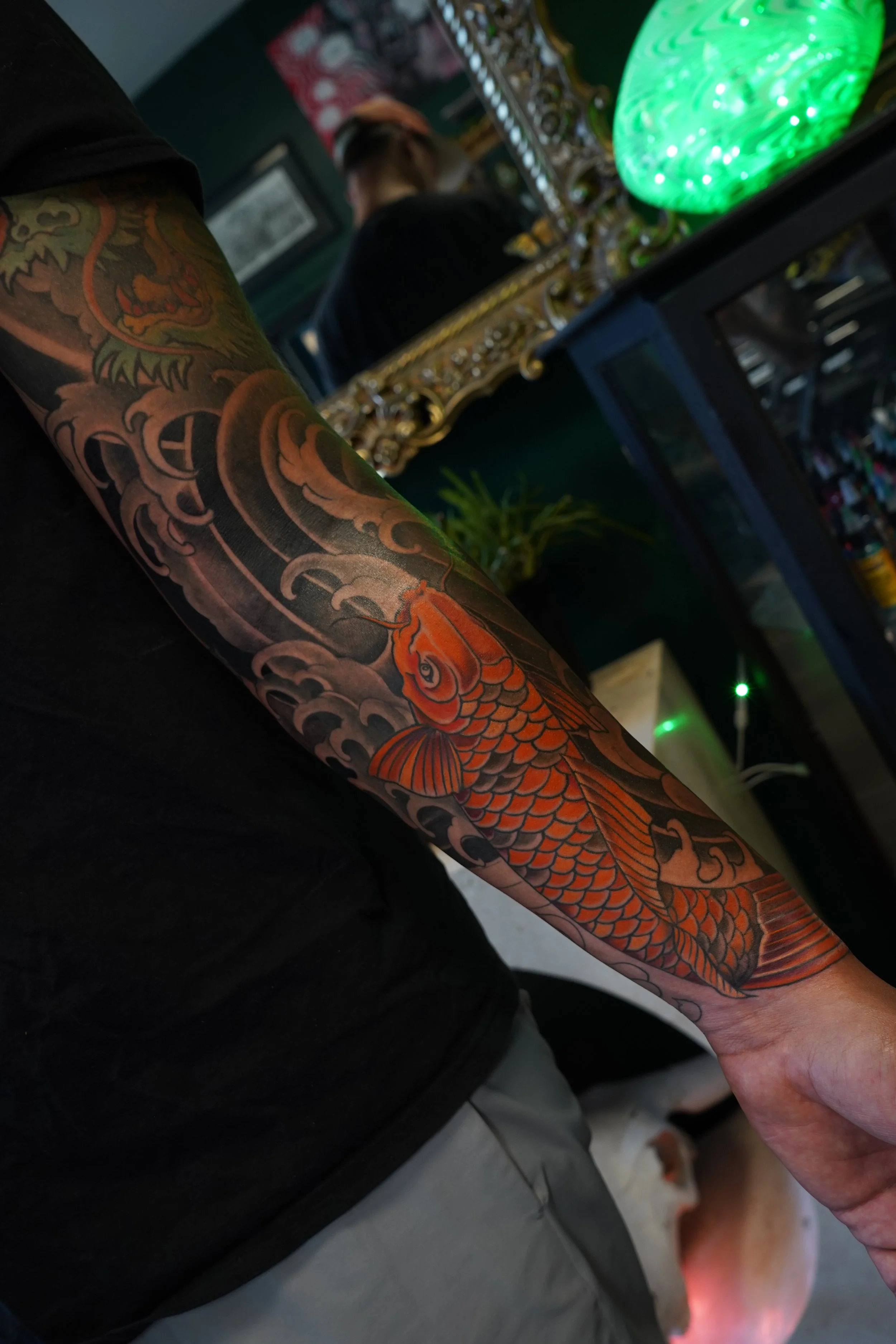 Tattoo of a koi fish on a person's arm, with dark clouds and a dragon in the background, taken inside a tattoo shop.