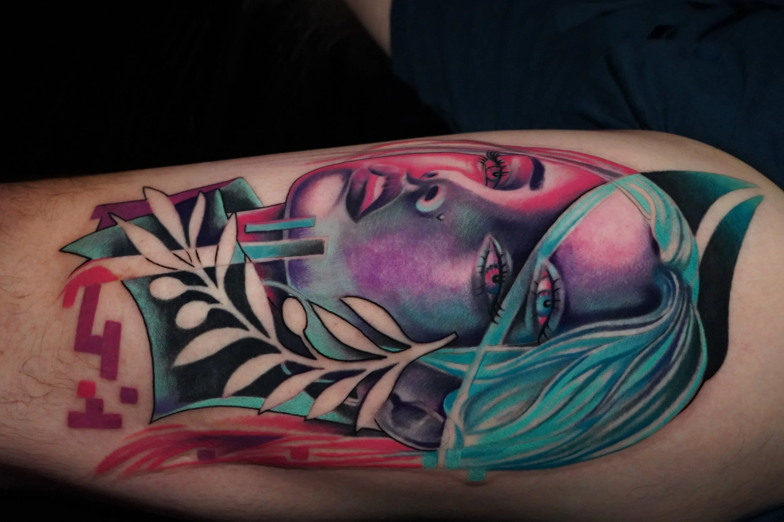 Colorful tattoo of a woman's face with blue hair, floral and geometric elements, on a person's arm.