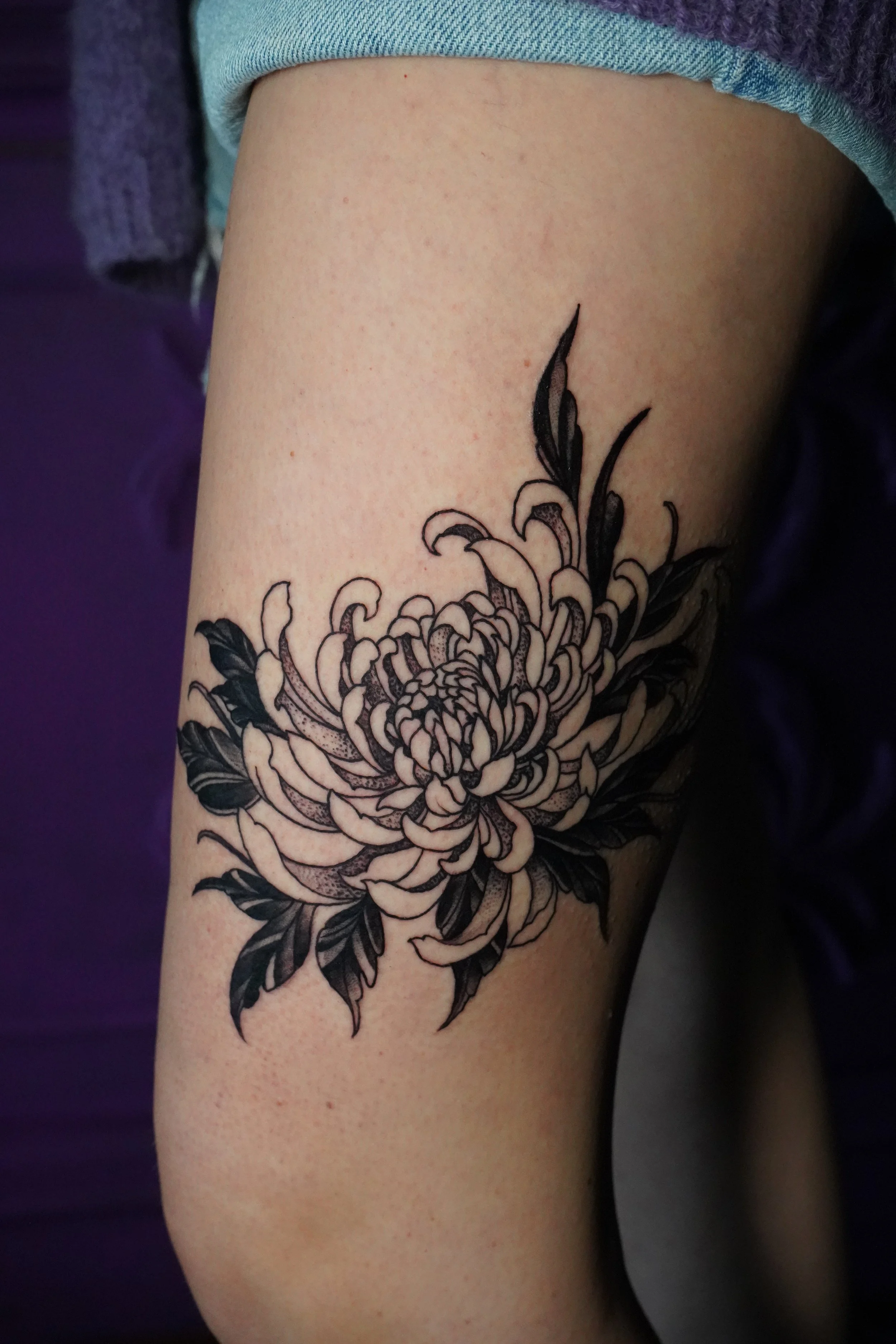 Black and gray floral tattoo of a large chrysanthemum on person's upper arm.
