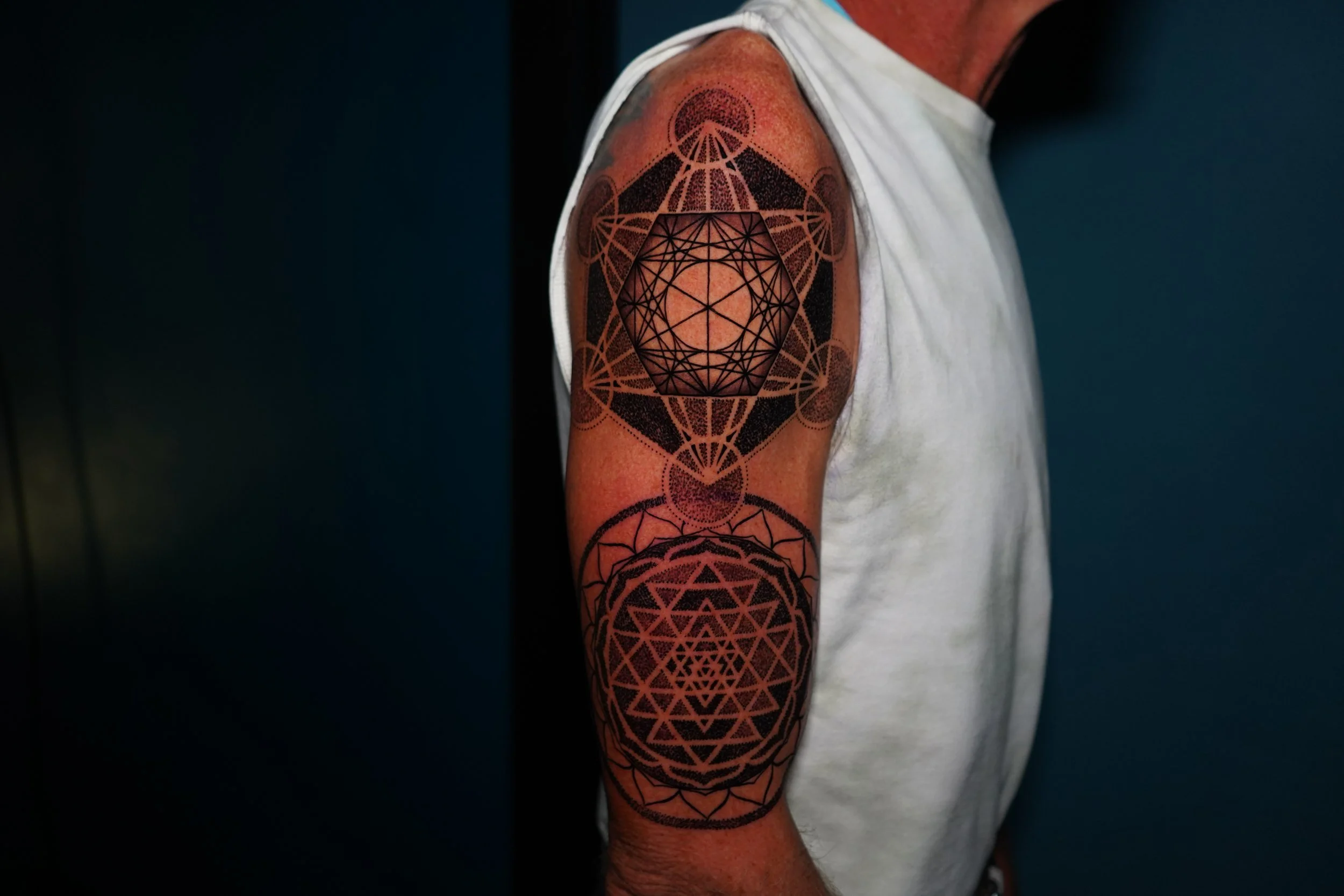Tattoo of geometric patterns on a person's arm, including a central black circle with interconnected lines and shapes, surrounded by intricate designs.