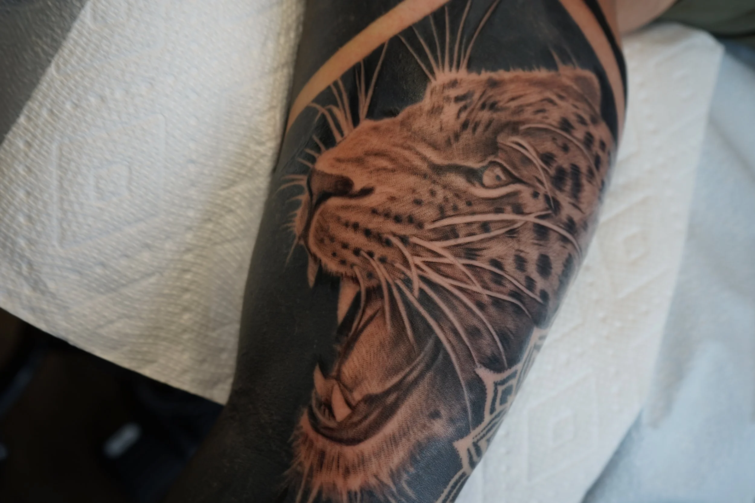 Tattoo of a lion's head on person's arm with detailed black and gray shading.