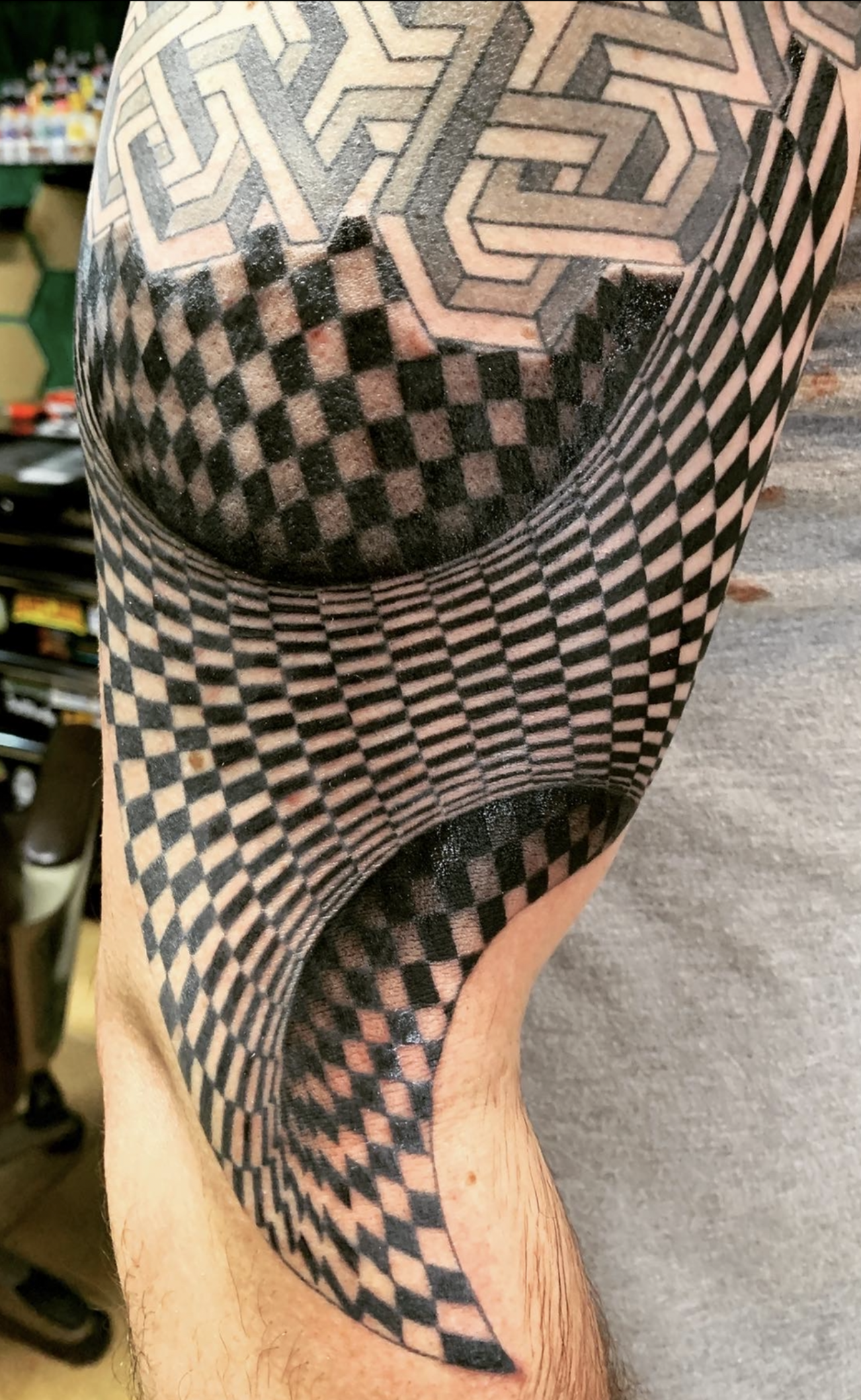 Close-up of a person's arm with a black and gray optical illusion tattoo creating a 3D tunnel effect.