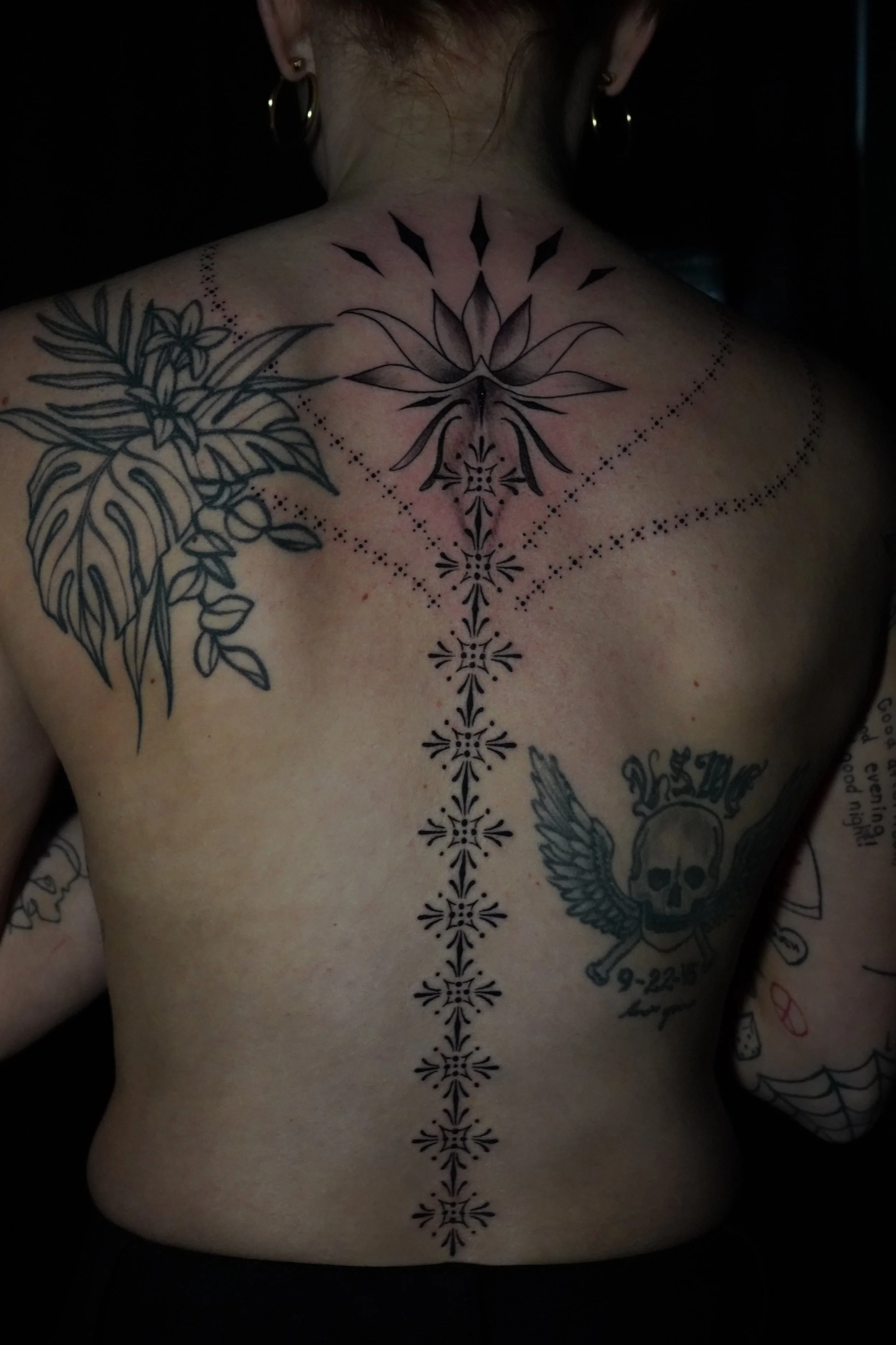 Back tattoo with floral and geometric designs, skull with wings, and dotted patterns.
