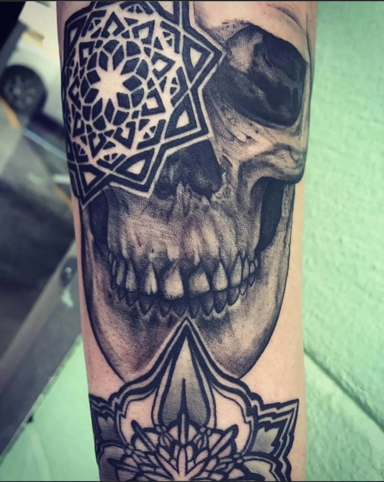 Tattoo of a realistic skull, geometric patterns, and mandala designs on arm.