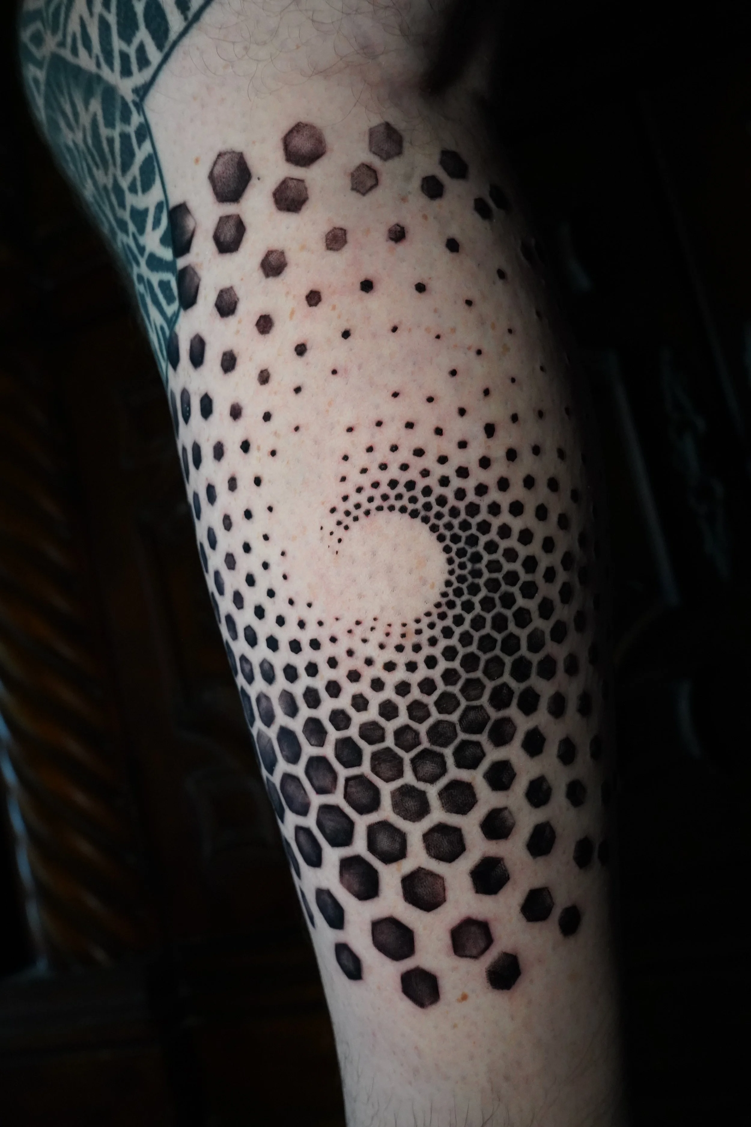 Tattoo of a hexagonal pattern forming a swirling spiral on a person's arm.