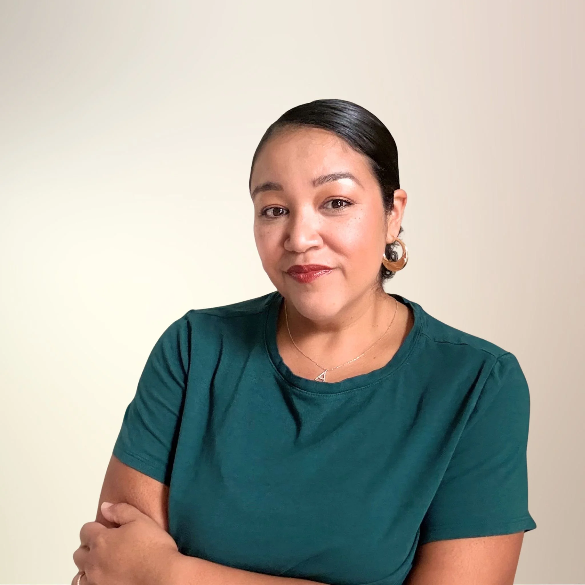 A woman with short dark hair, earrings, and a green shirt standing against a plain light-colored background.