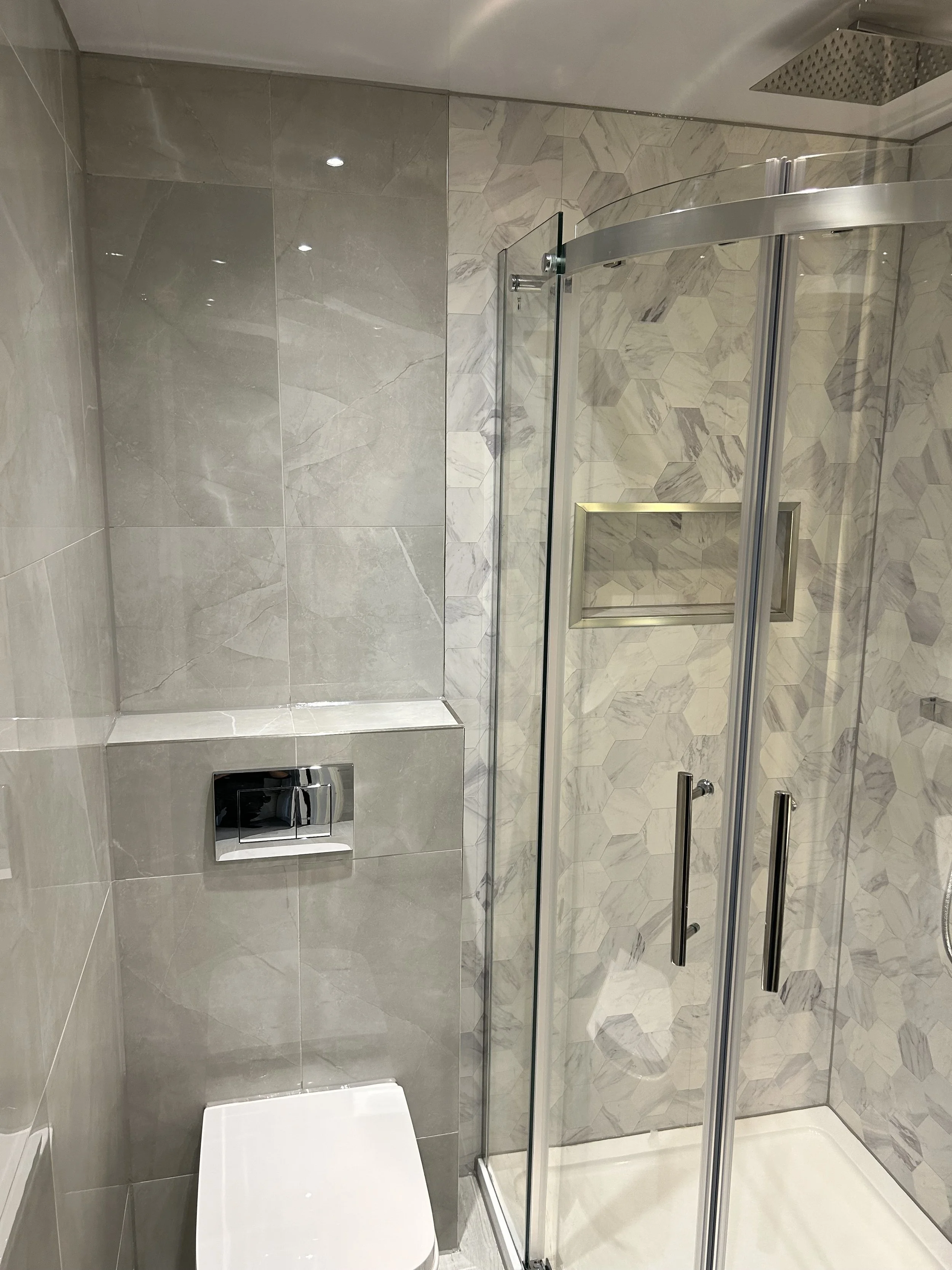 A modern bathroom featuring a toilet and a glass shower stall with hexagonal tile walls.