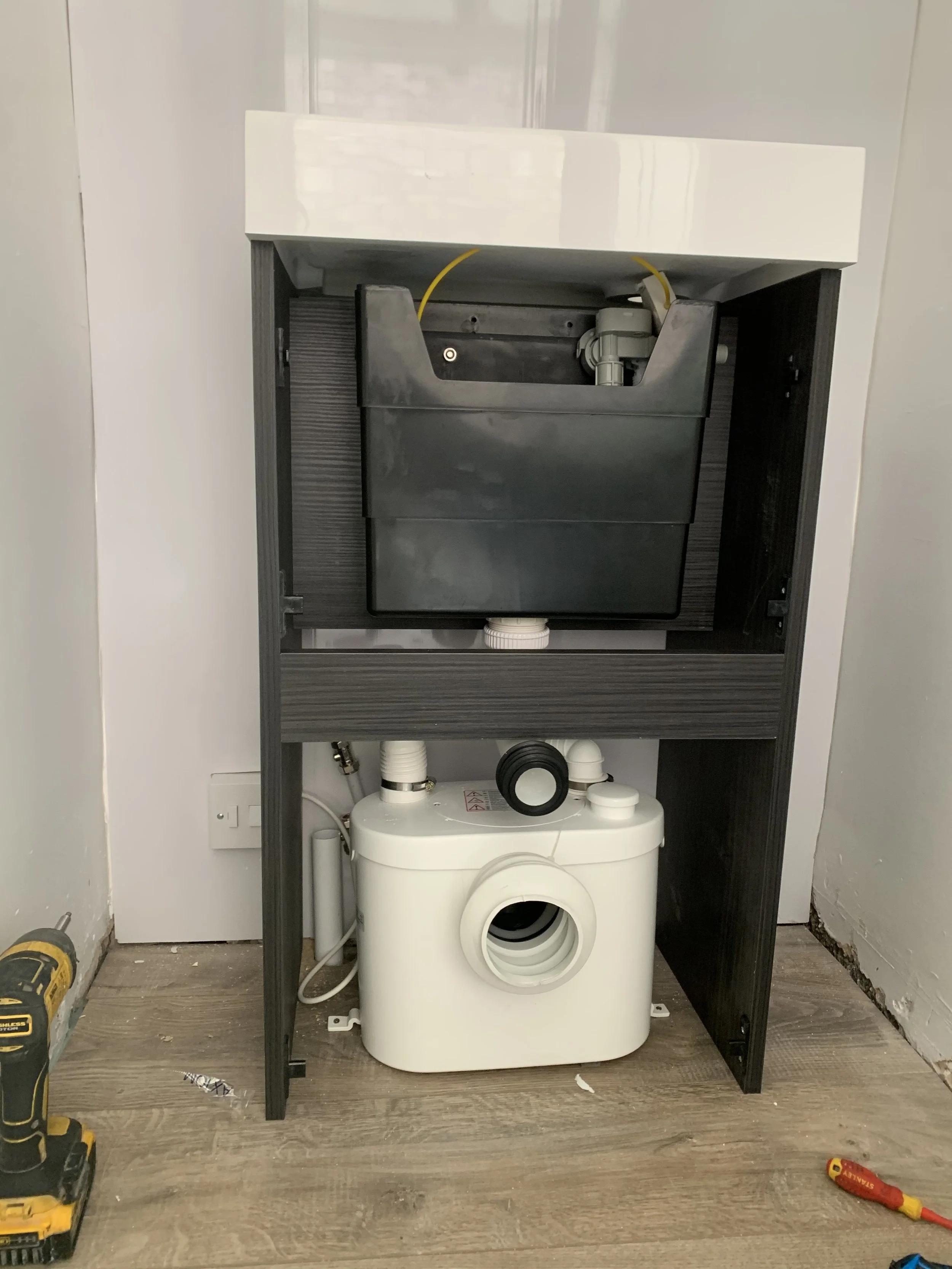 Under-sink plumbing and a water pump installation with black and white pipes, a black tank, and tools nearby.