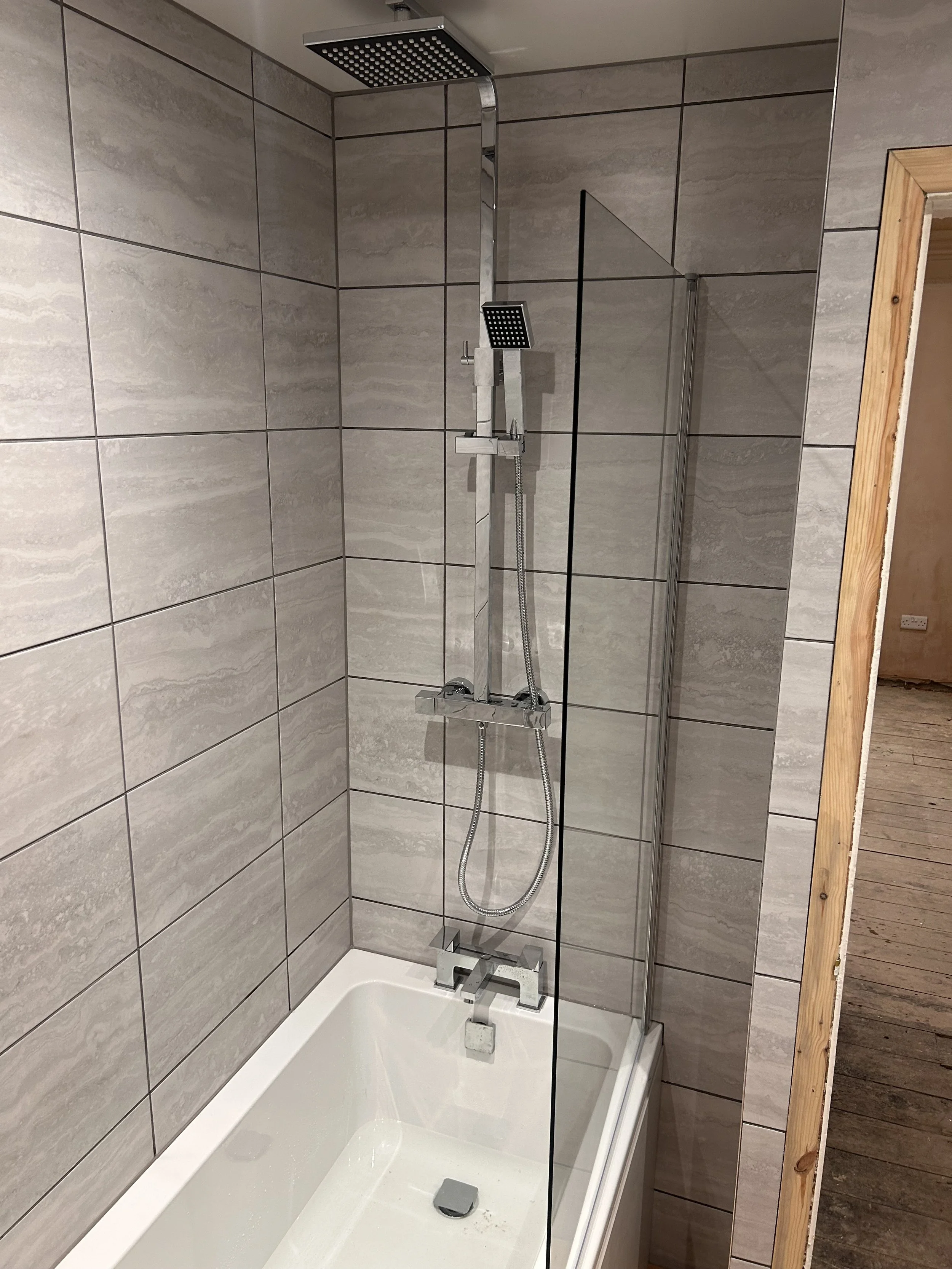 Modern bathroom shower with a rainfall showerhead and a handheld showerhead, glass partition, and tiled walls.