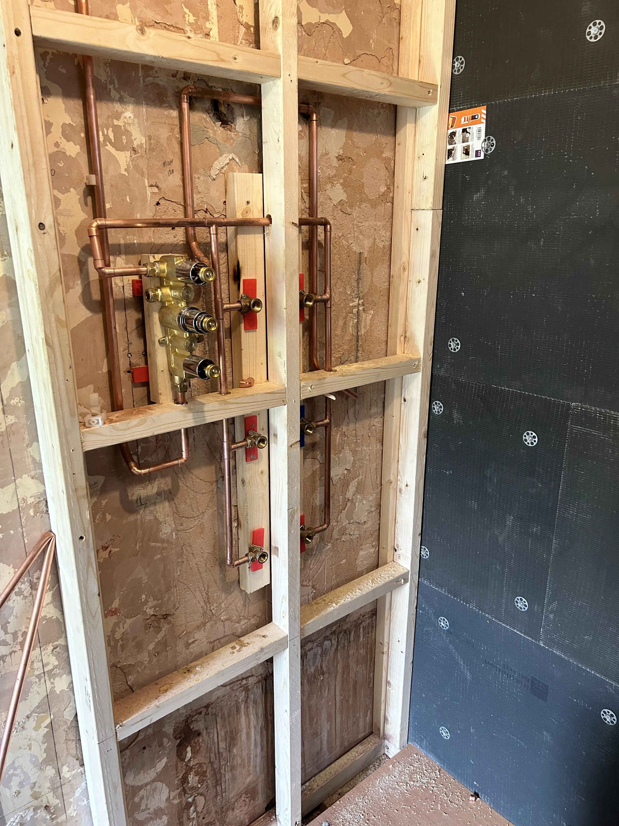 Copper plumbing pipes and fittings inside a wooden framing wall, which appears to be part of a plumbing installation for a bathroom or kitchen.
