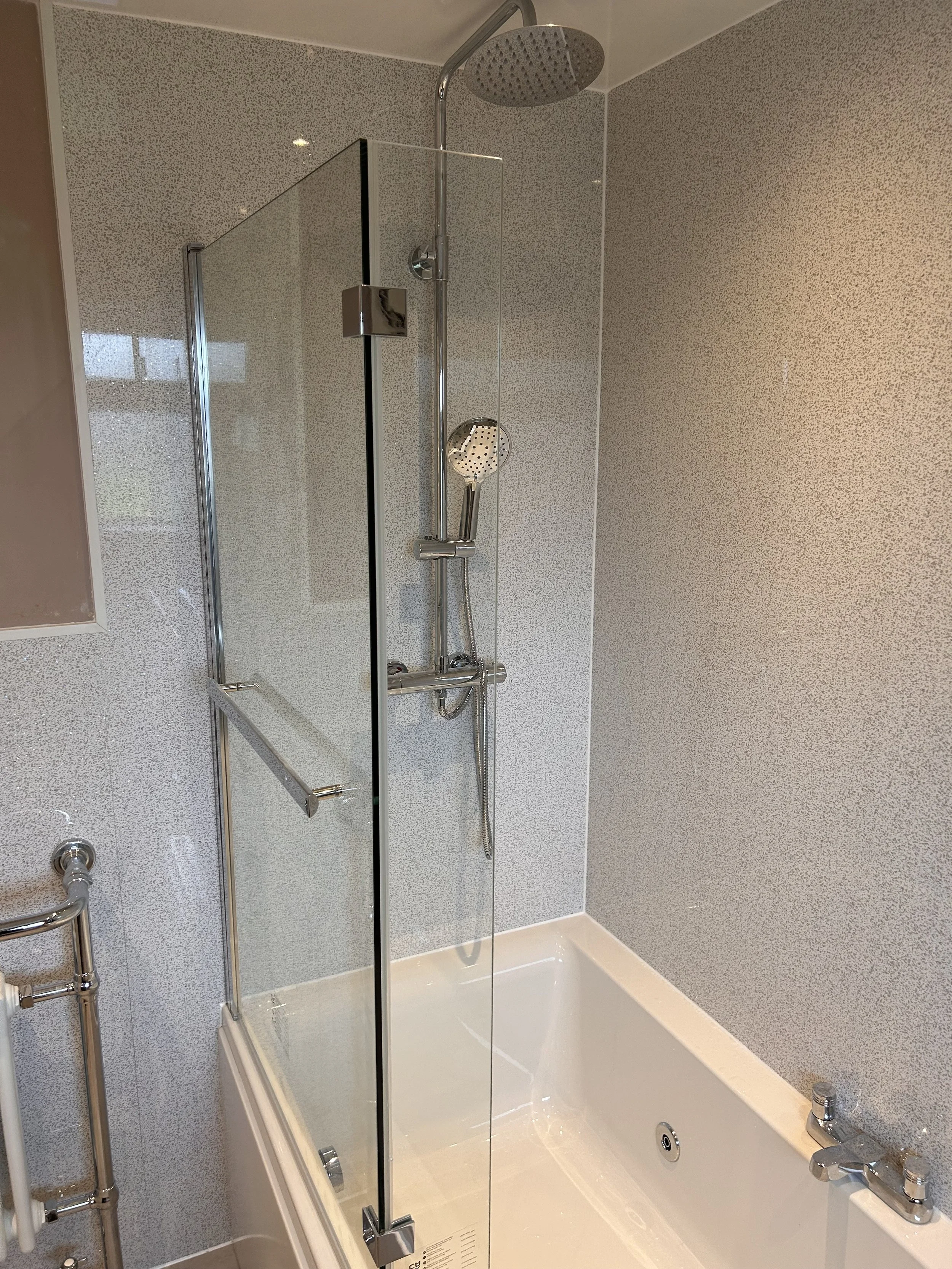 A modern bathroom shower with a glass door, a large overhead rain showerhead, a handheld shower, and a built-in bathtub.