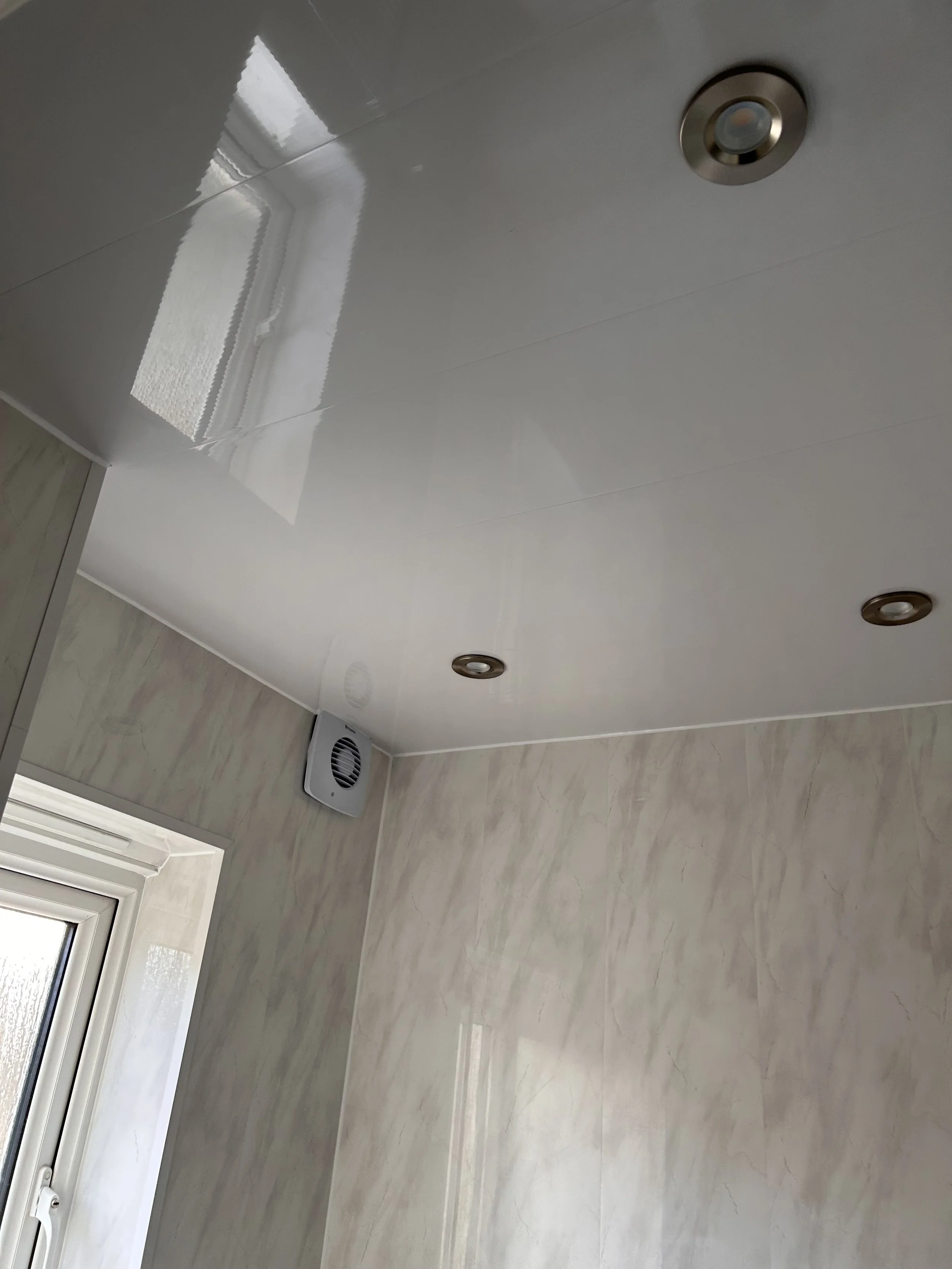 Ceiling with recessed lights and a ventilation fan, part of a room with a recessed window and beige wall with a marble-like finish.
