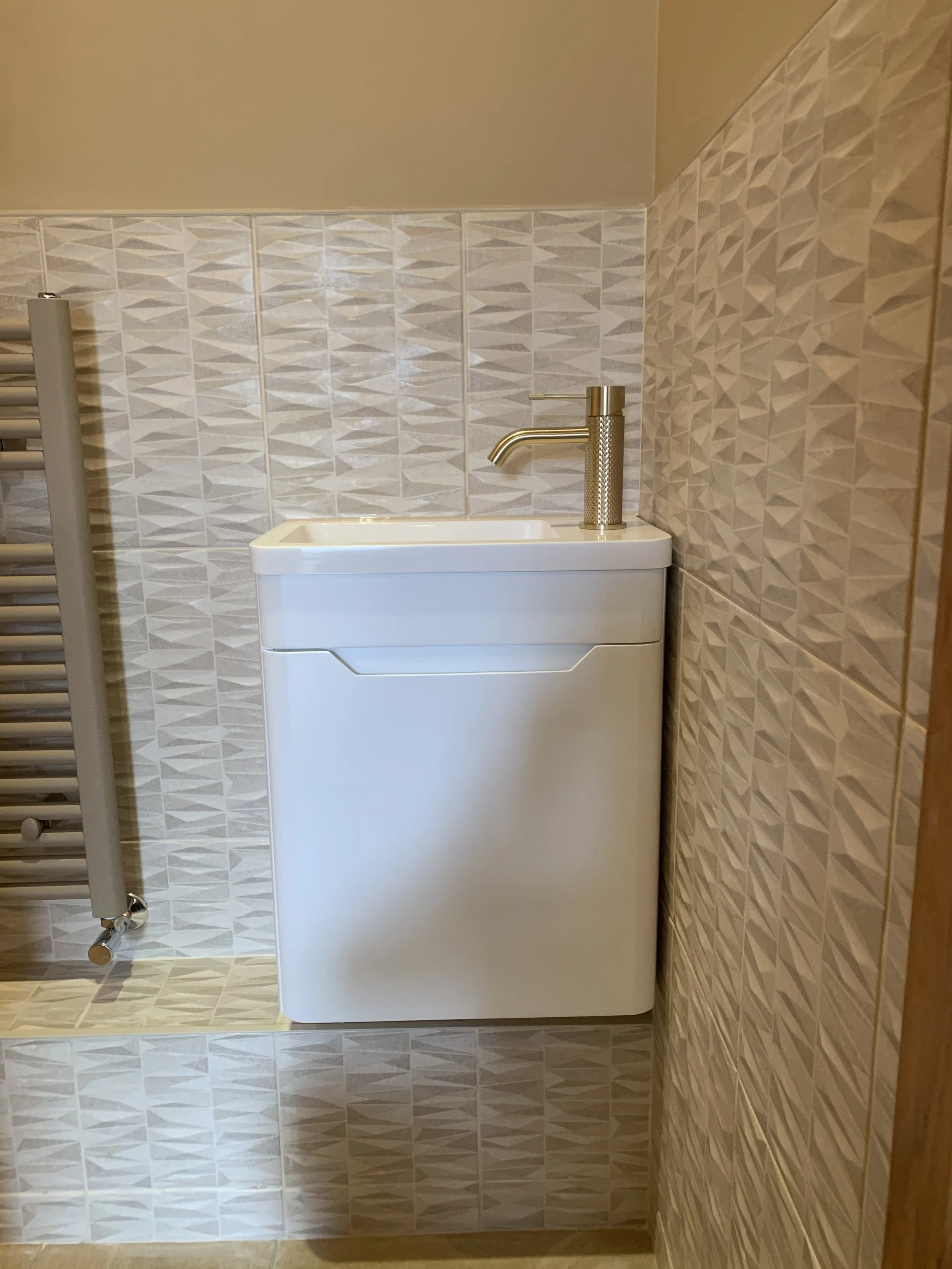 Small white sink with a brass-colored faucet next to a tiled wall in a bathroom or utility room.