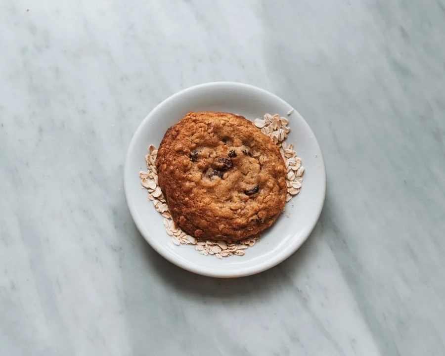 Chocolate chip cookie on a white plate with oatmeal flakes, on a marble surface.