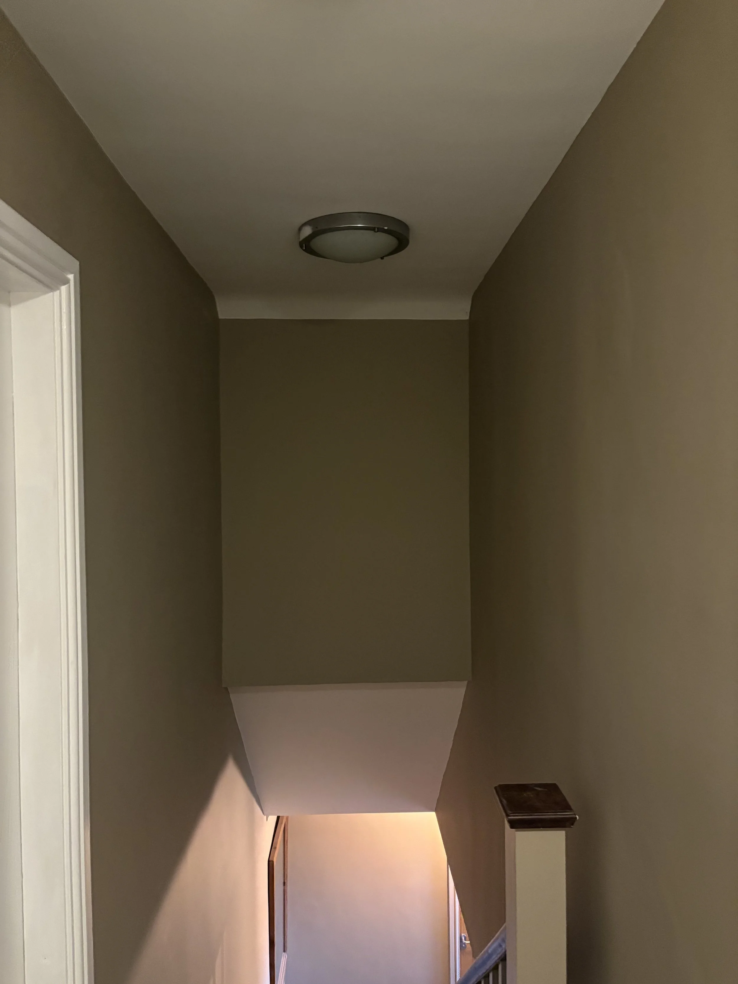 Hallway with beige walls, ceiling light, staircase, and door at the end