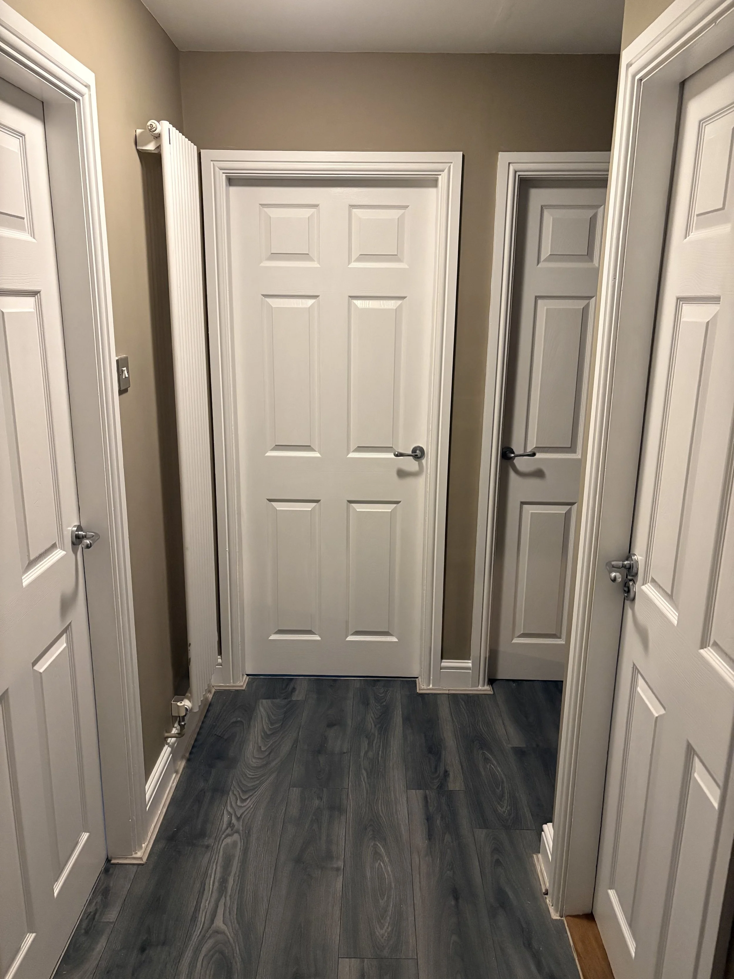 A hallway with beige walls, white doors, and dark wood flooring.