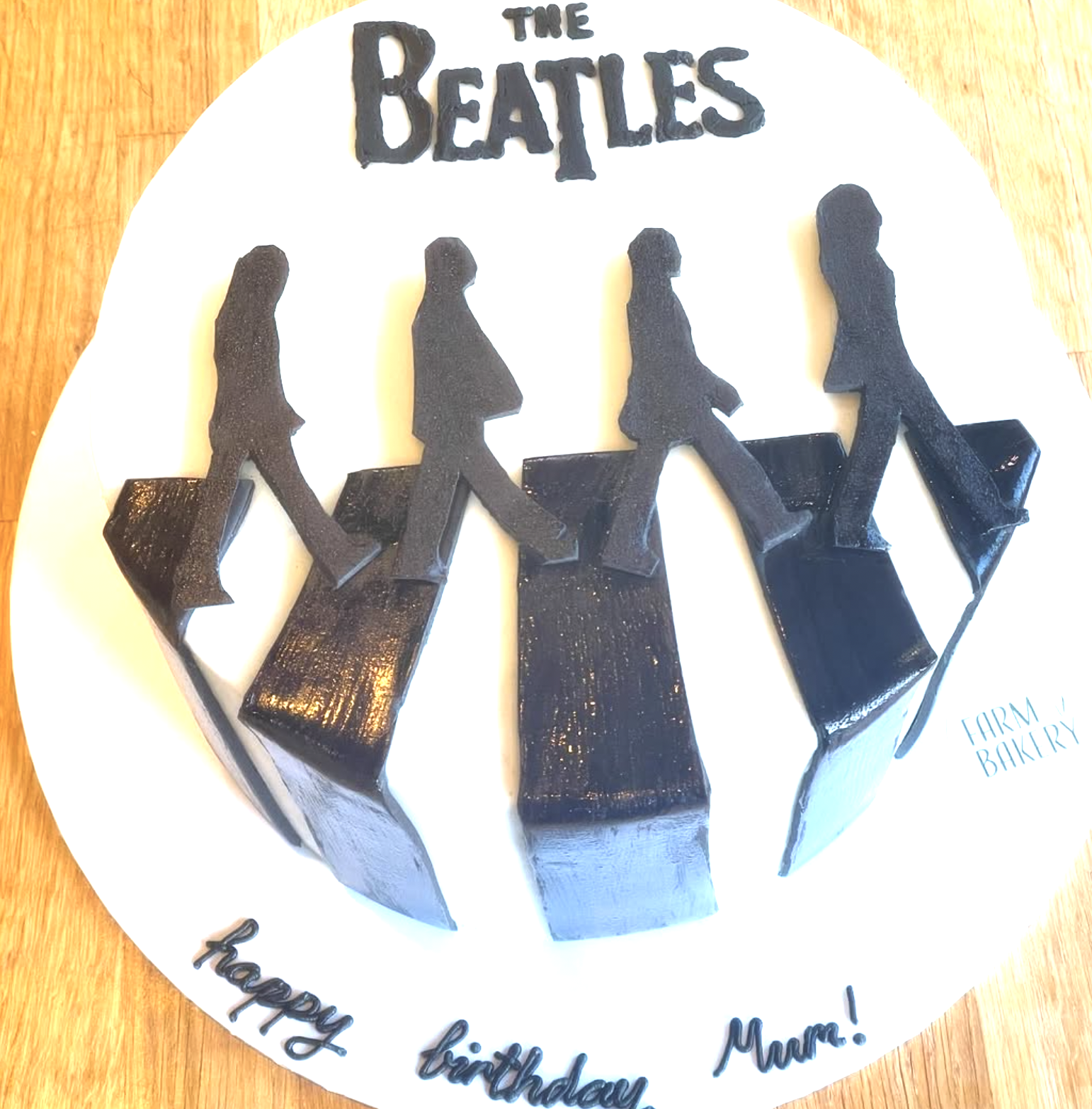 Clockwise from bottom left: birthday cake with a cake topper featuring the Beatles walking across Abbey Road on black fondant silhouette figures, with a message that reads, "happy birthday MUM!" and "FARM BAKERY" in blue text.