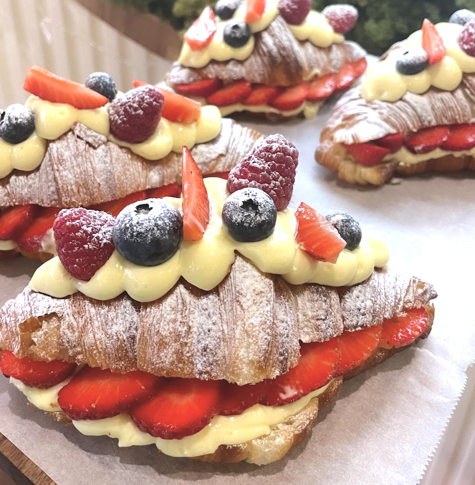 Eclairs topped with berries and cream, filled with strawberries and cream, dusted with powdered sugar.