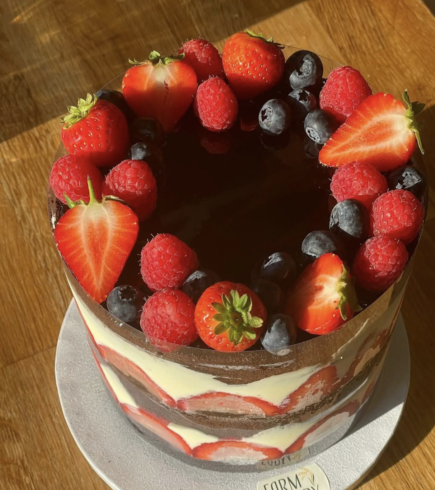 Chocolate cake decorated with strawberries, raspberries, and blueberries on top, placed on a white board on a wooden surface.