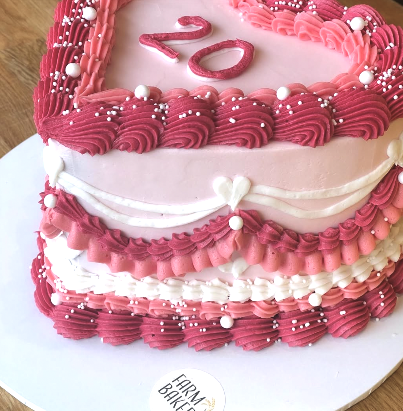 A heart-shaped birthday cake decorated with pink and white frosting, pearls, and swirl piped icing, with the number 21 written on top.