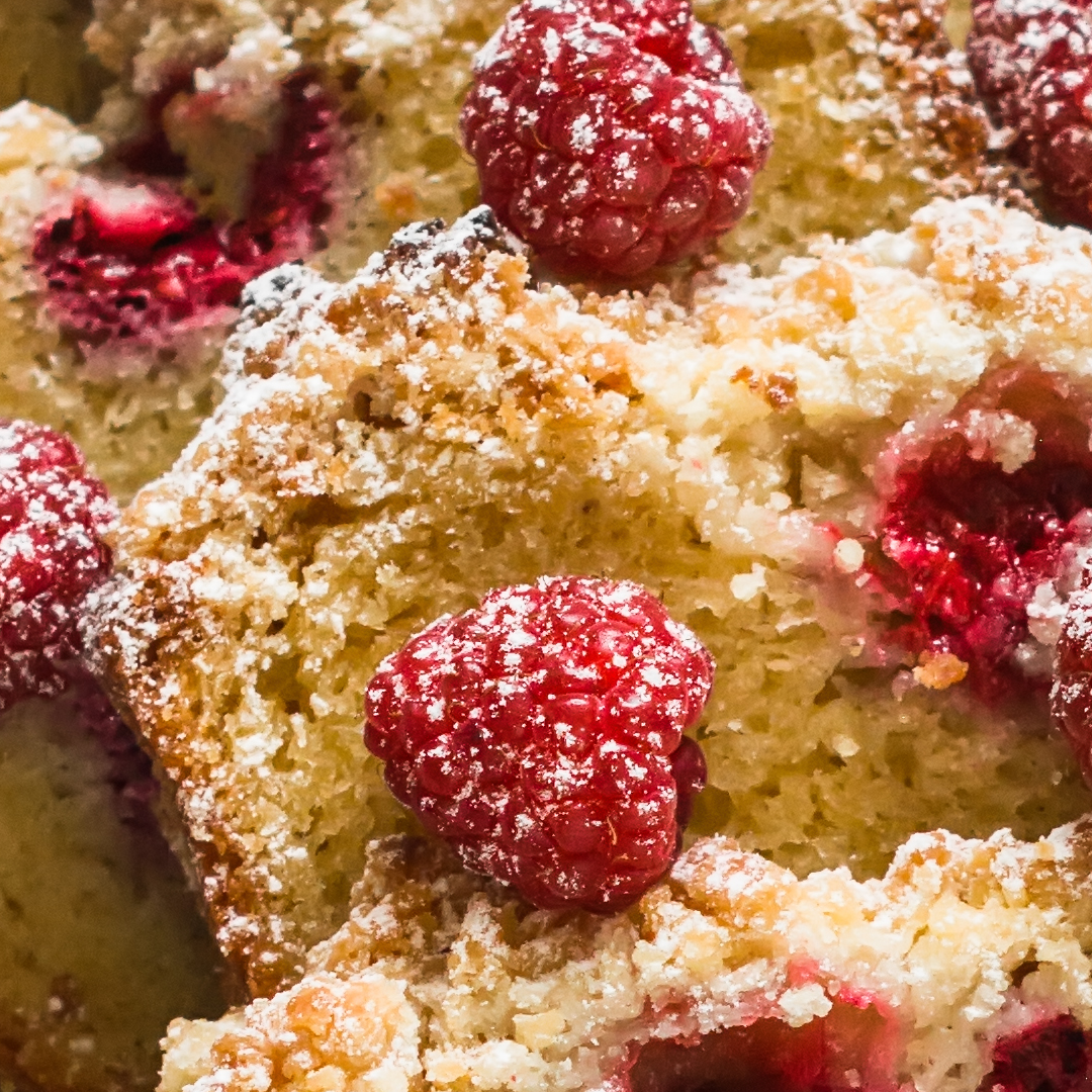 Close-up of a dessert with raspberries, crumbled topping, and powdered sugar.