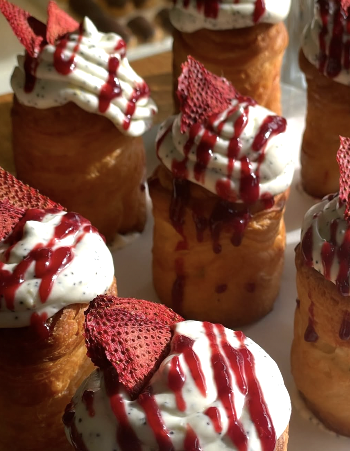 Close-up of strawberry shortcake cupcakes with whipped cream, strawberry slices, and red drizzle on top.
