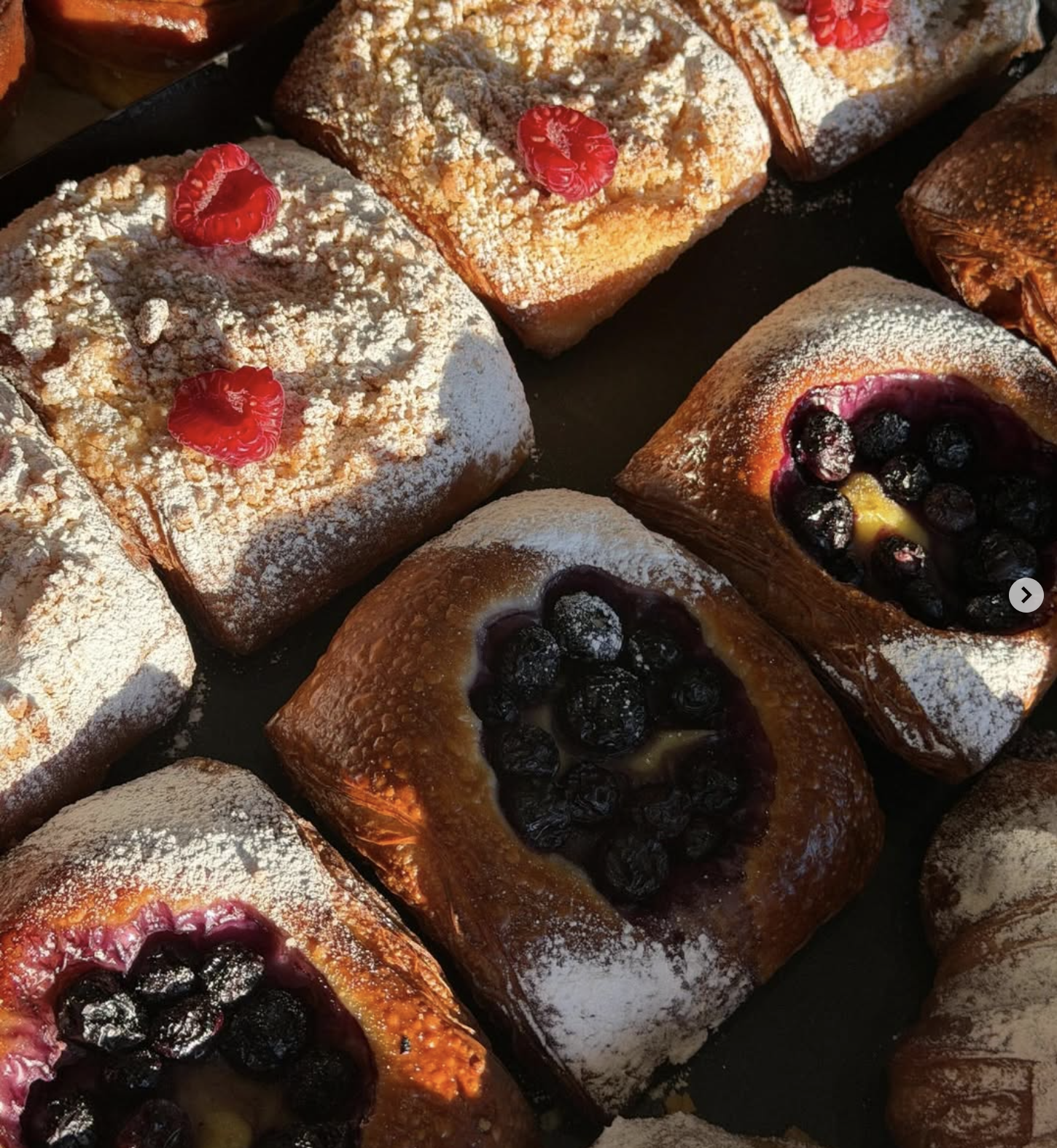 Assorted Danish pastries with powdered sugar, raspberries, and blueberries.